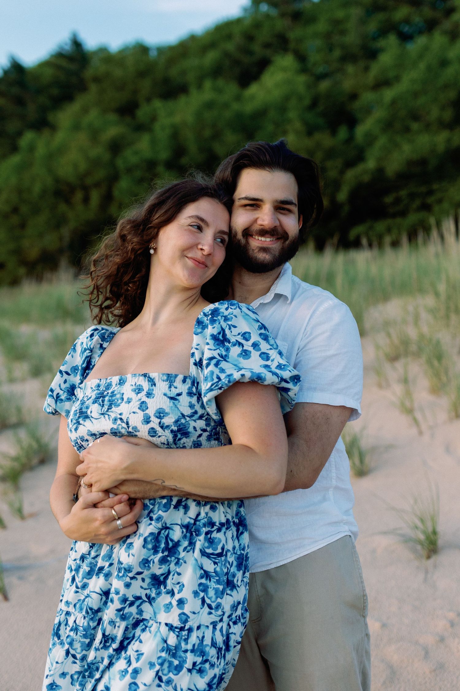 Couple embraces on sandy dunes wearing casual summer outfits.