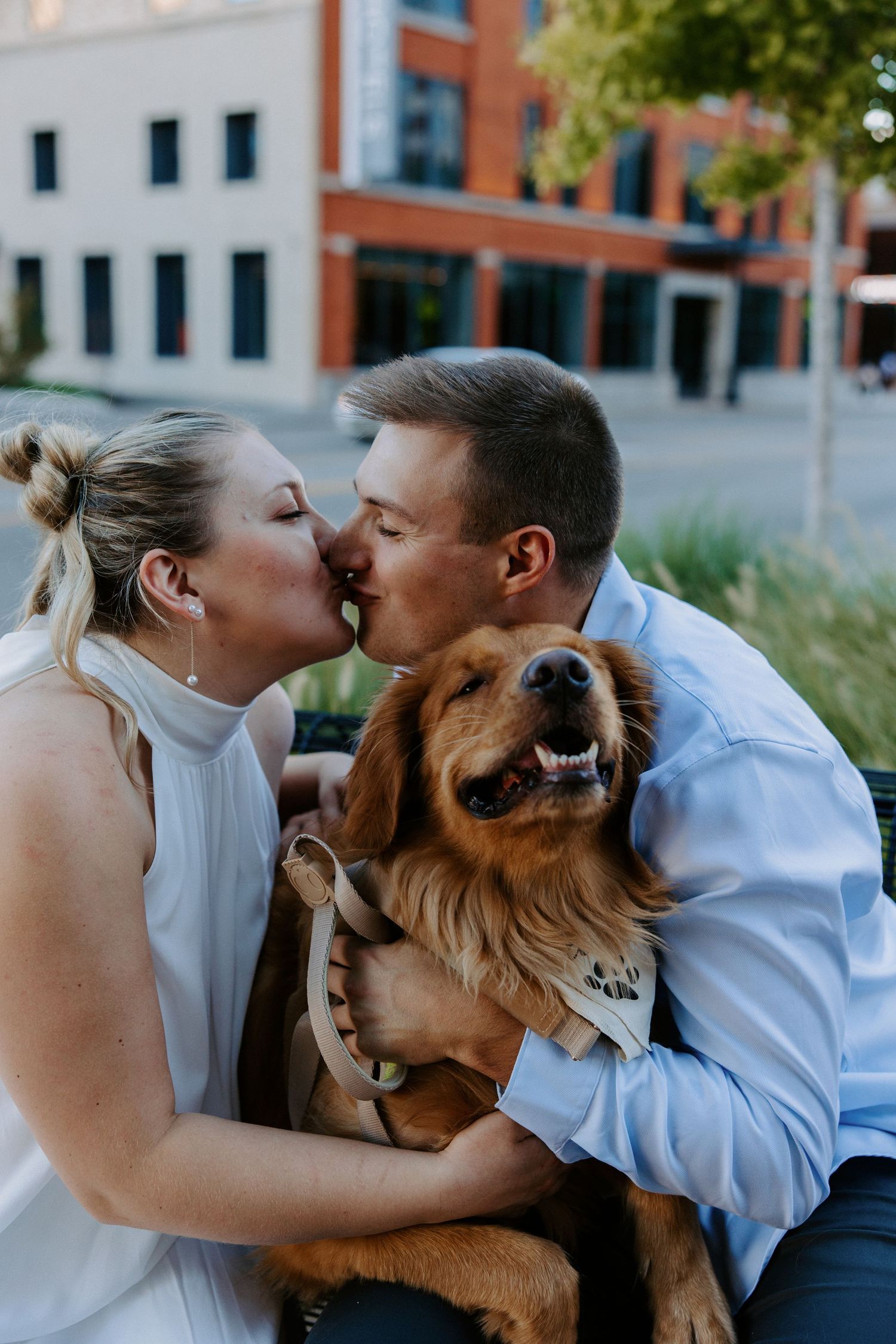 A couple shares kisses with their happy golden retriever dog outdoors.