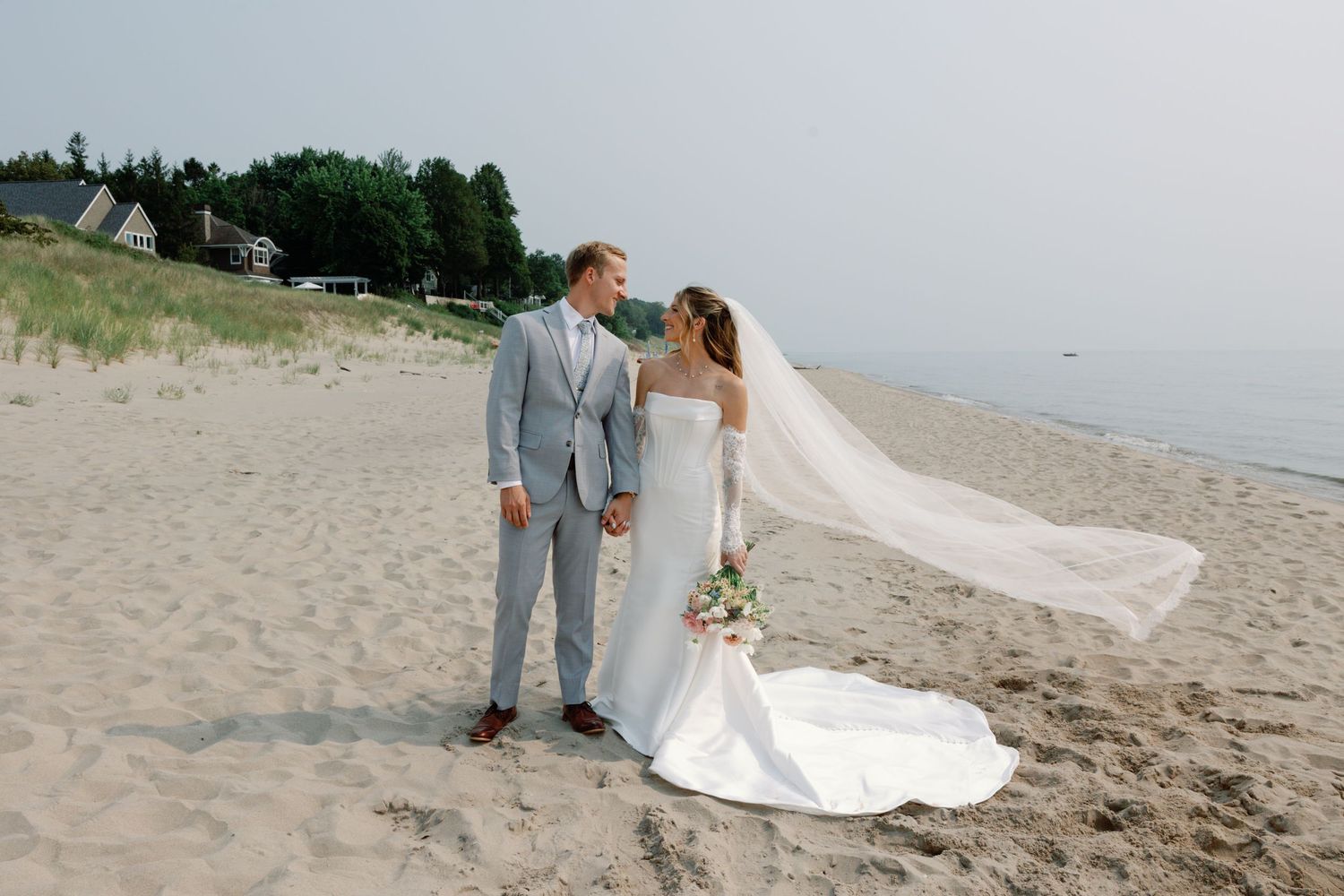 Couple in wedding attire walking along scenic beach shoreline.
