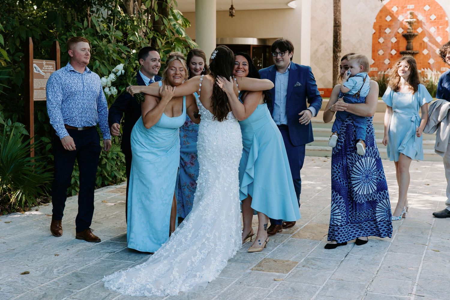 Wedding party in blue dresses and formal attire poses on a columned patio.