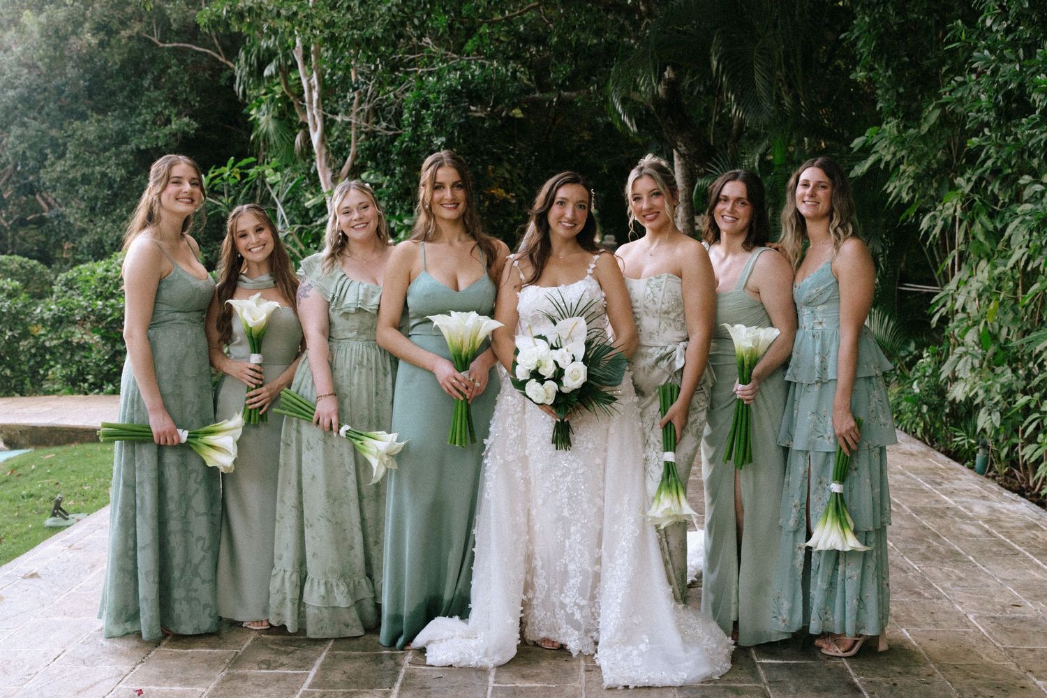 Wedding party in sage green dresses posing together in a garden setting.