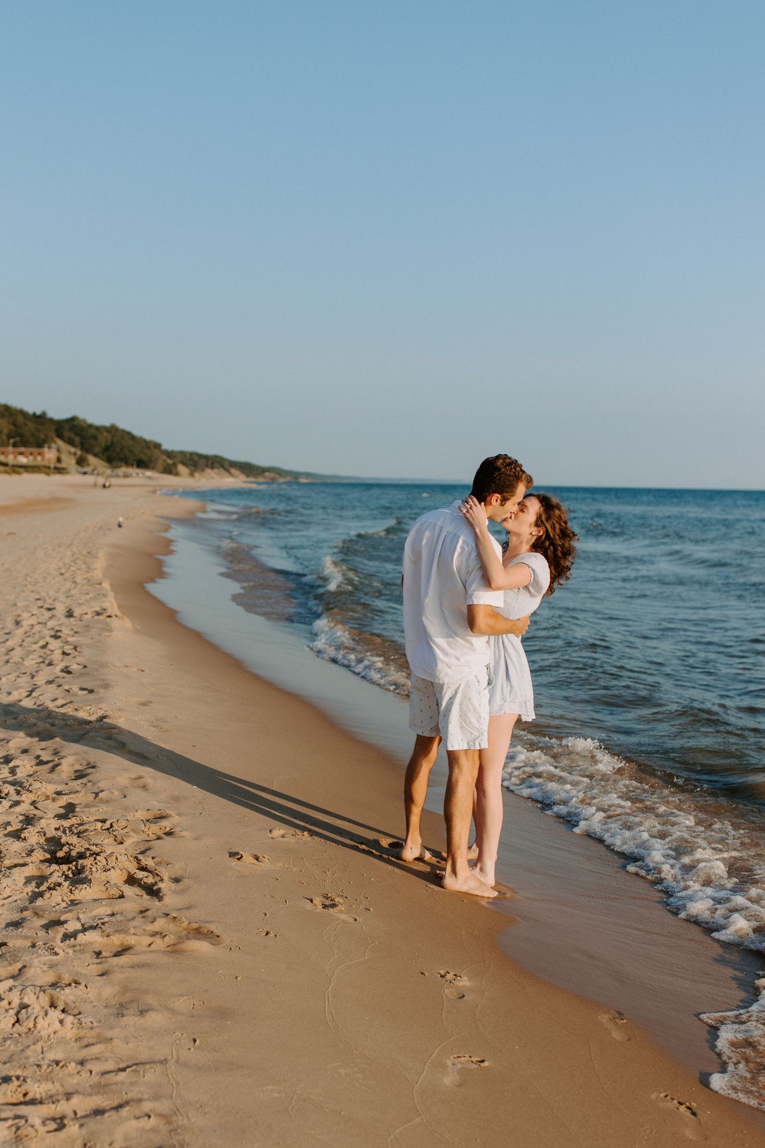 Romantic couple shares intimate moments on a sandy beach during golden hour.