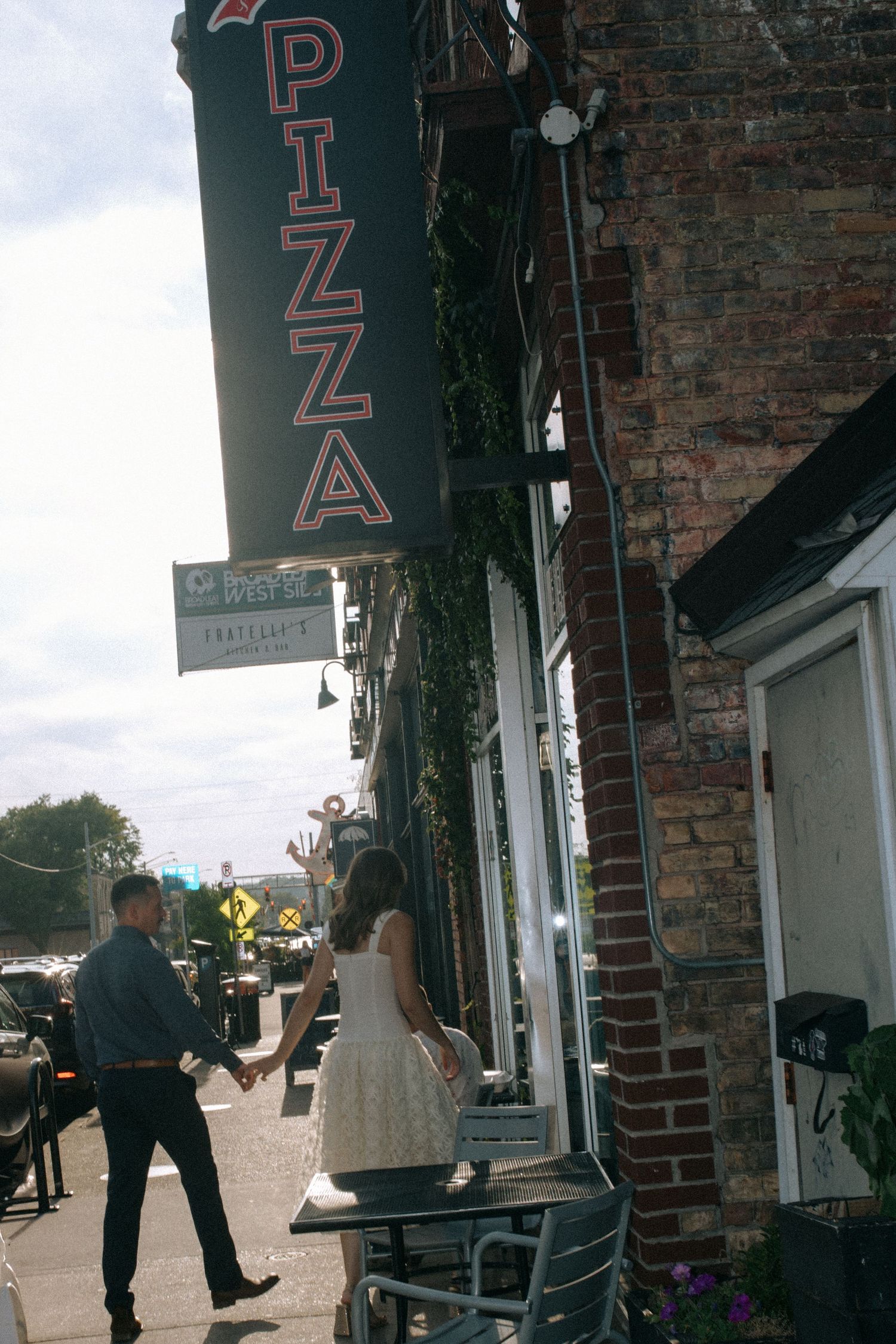 Casual engagement photos outside a brick building with storefront signage.