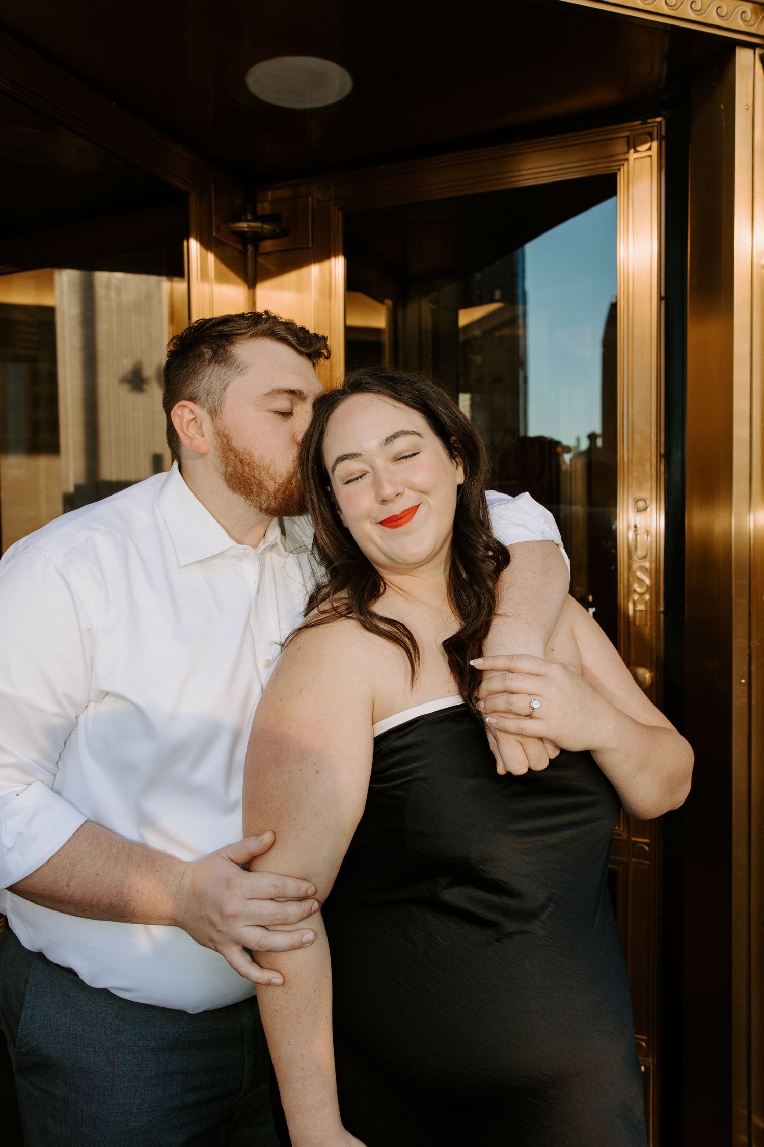 A romantic couple embraces in a warmly lit hallway with elegant architectural details.