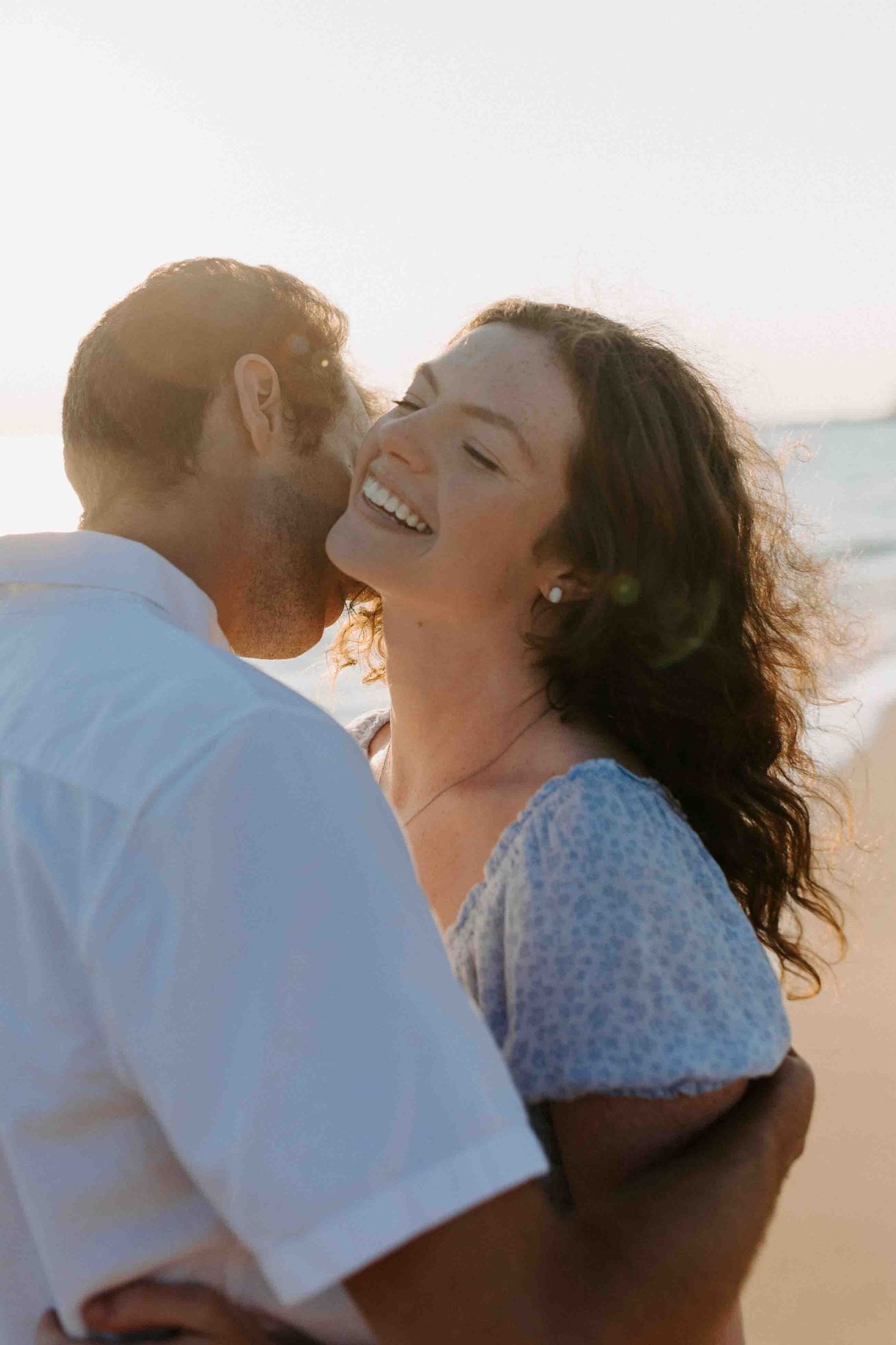 Couple sharing playful romantic moments on a sunny beach.