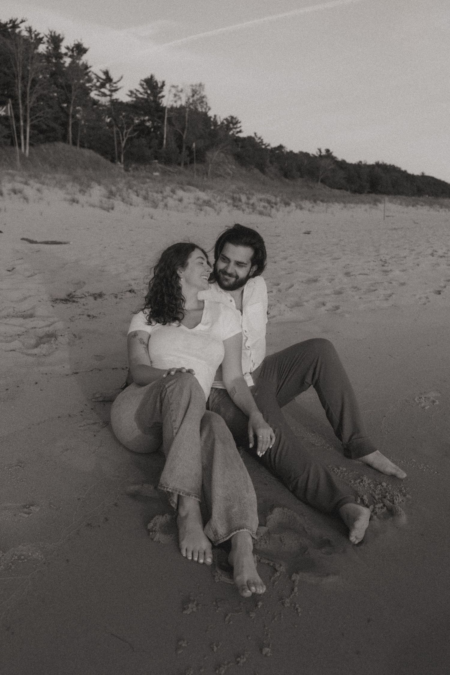Black and white photo of a couple lounging on beach sand at dusk.
