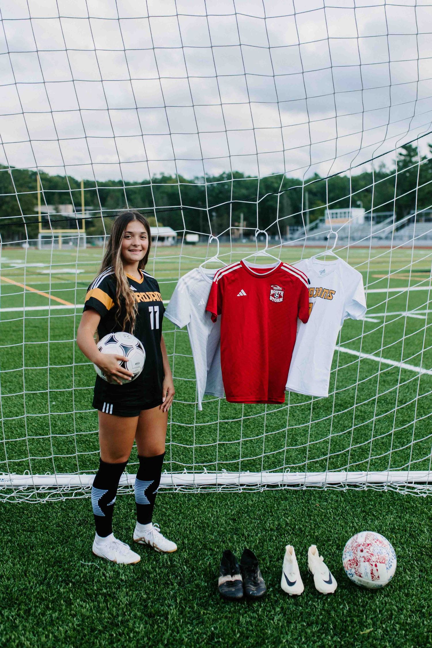 Soccer gear and uniforms arranged by goal post with player posing on field.
