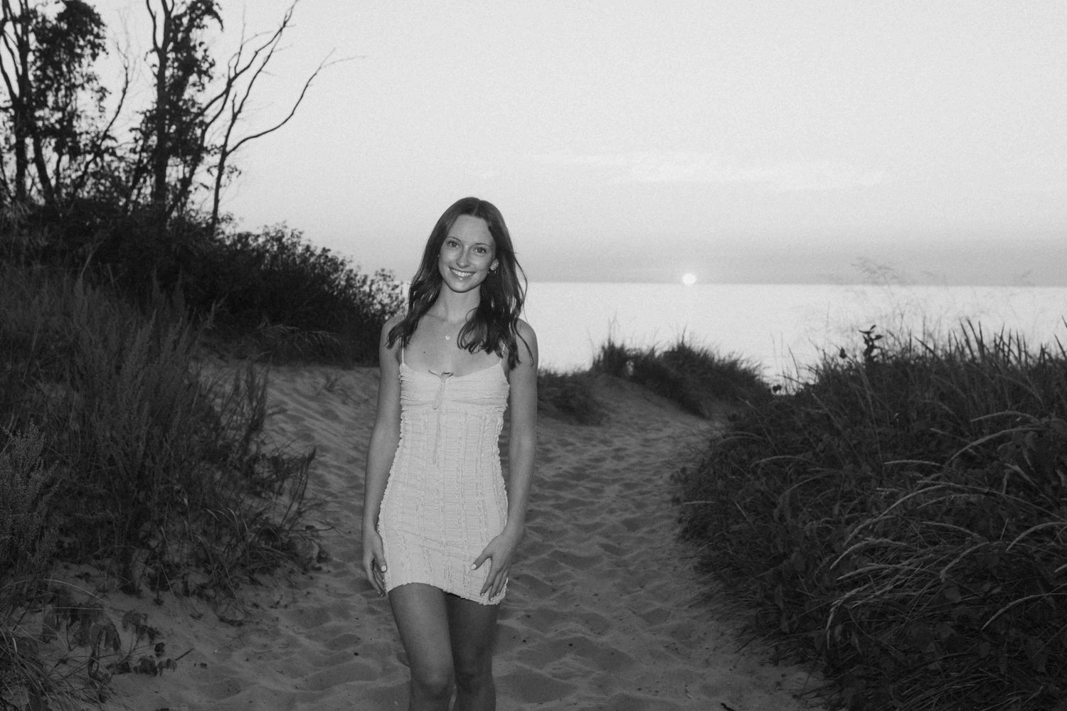 A group poses together on a sandy beach path at sunset with brush and dunes in the background.