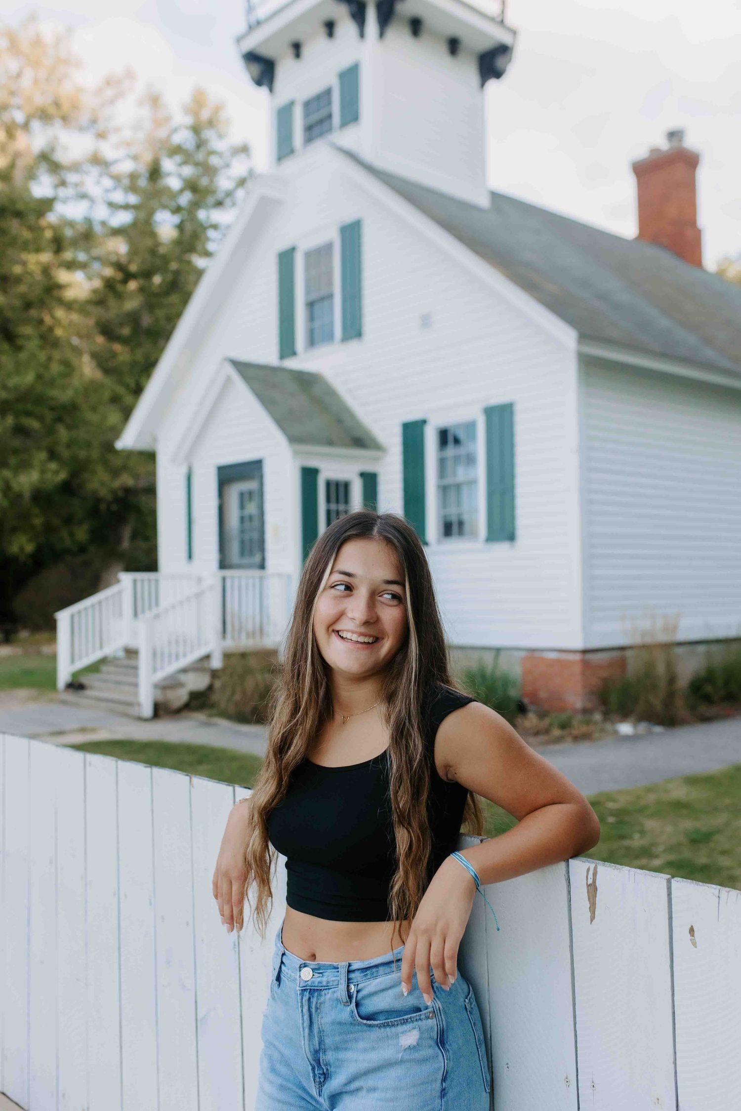 Candid poses by a classic white farmhouse with green trim and wooden fence.