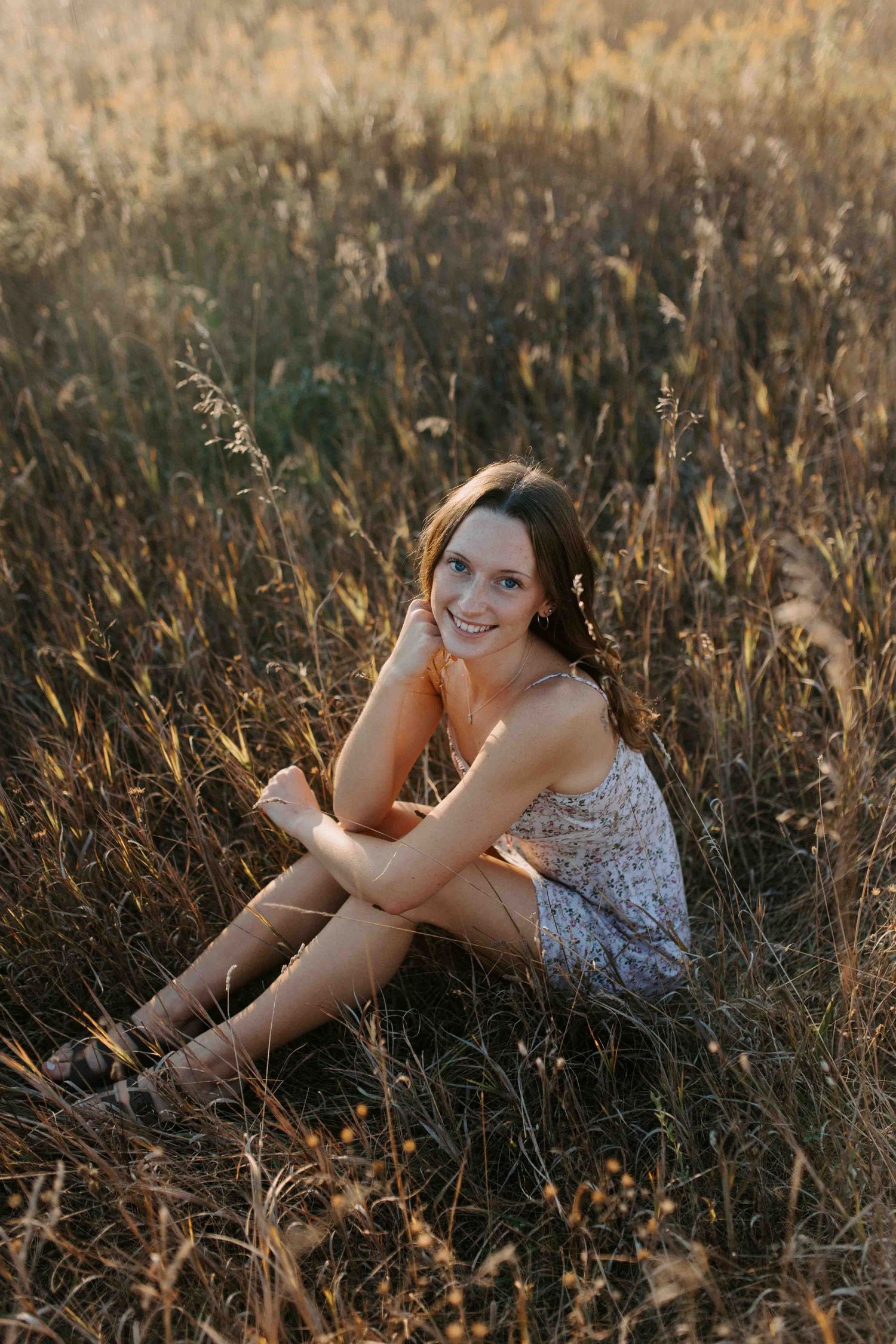 A floral dress-clad figure reclines in a golden field at sunset, creating a dreamy summer portrait.