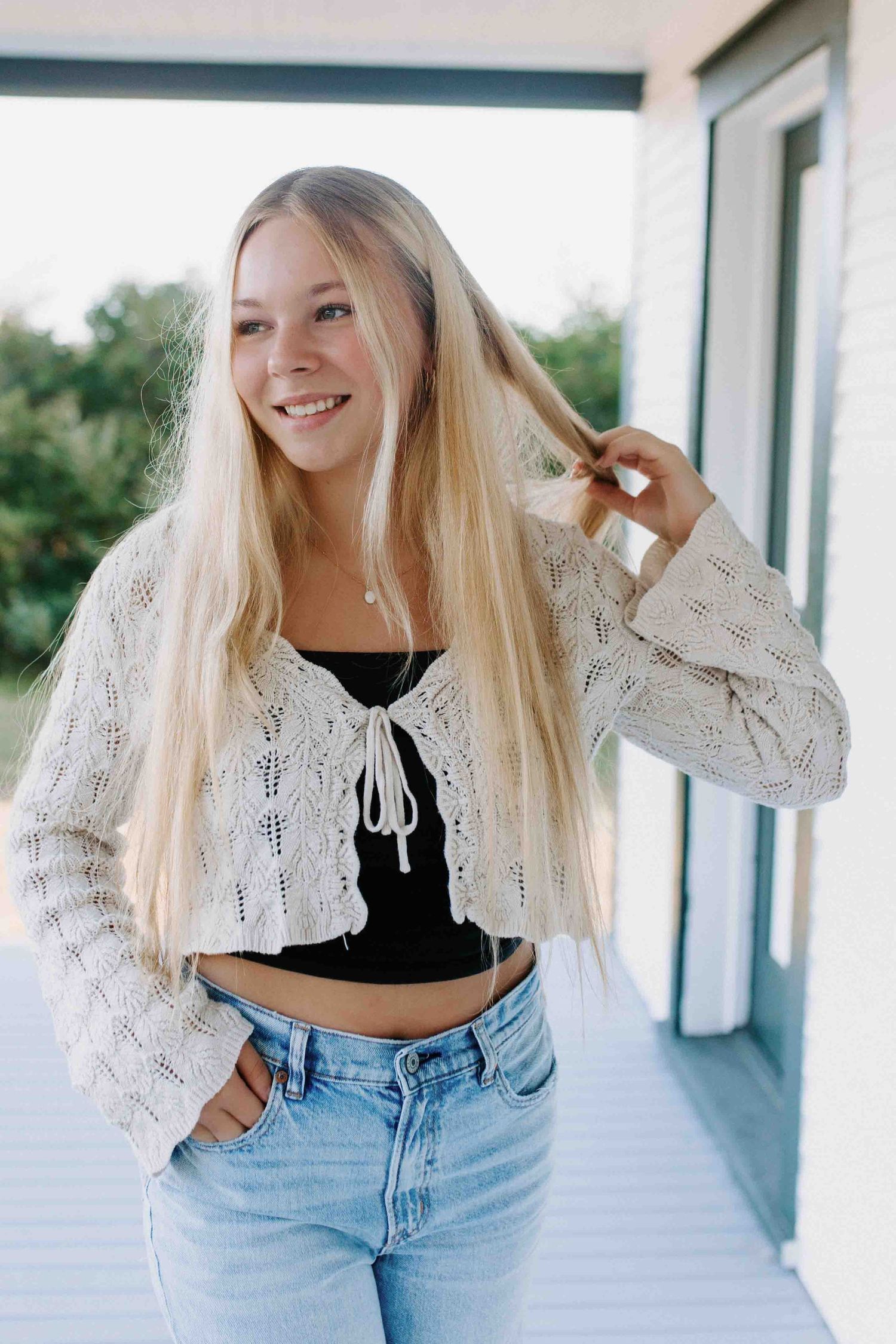 Candid shots on a farmhouse porch showing off a white knit cardigan and light wash denim outfit.