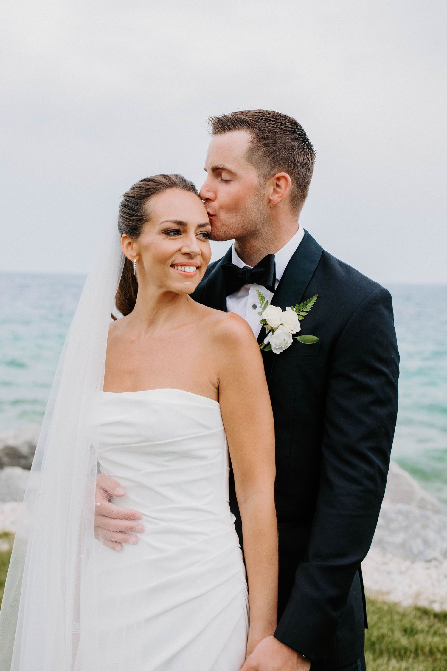 Seaside wedding portrait with turquoise ocean backdrop and white floral boutonniere detail.