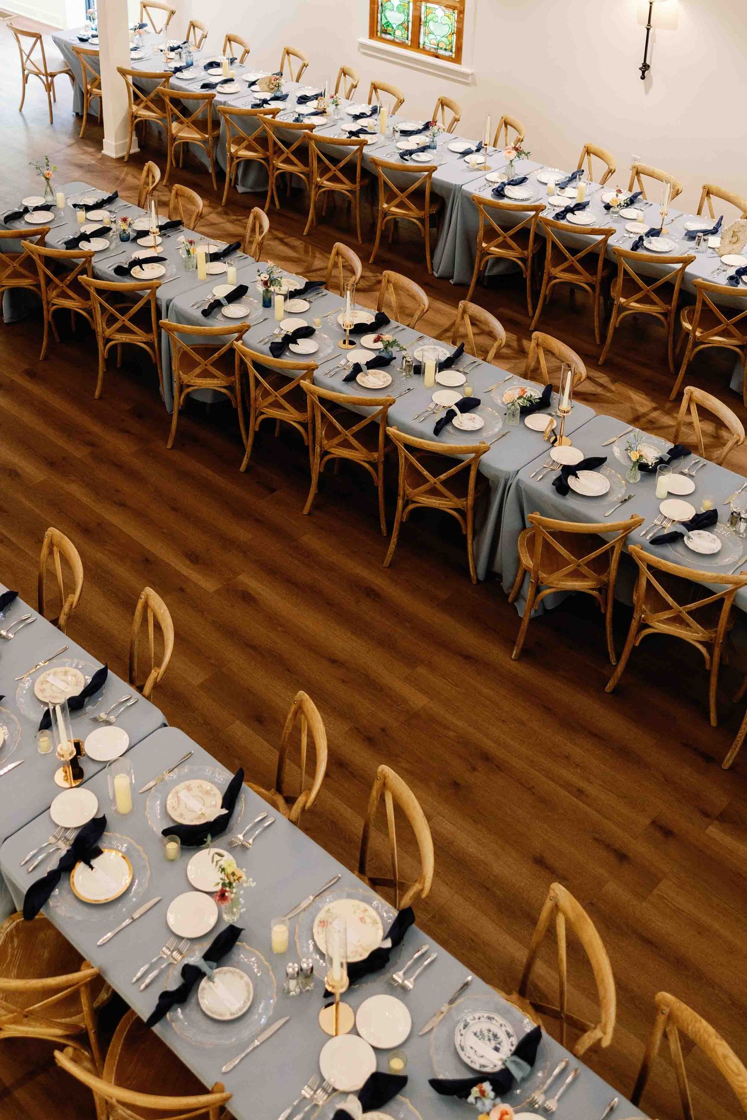 Wedding reception tables set with gray linens and wooden chairs in an elegant indoor venue.