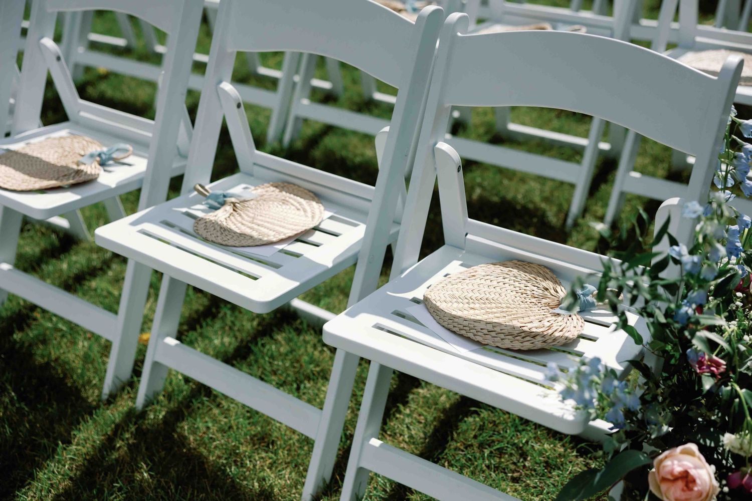 White wooden chairs arranged in rows on grass for an outdoor wedding ceremony.
