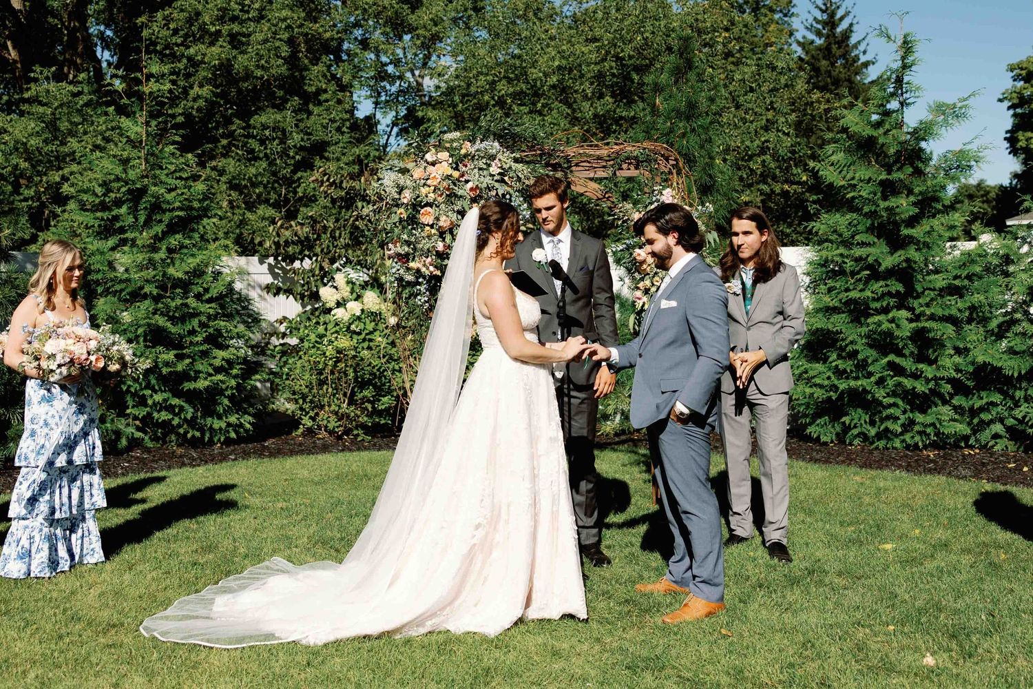 Wedding ceremony taking place on a sunny lawn with decorative floral arrangements.