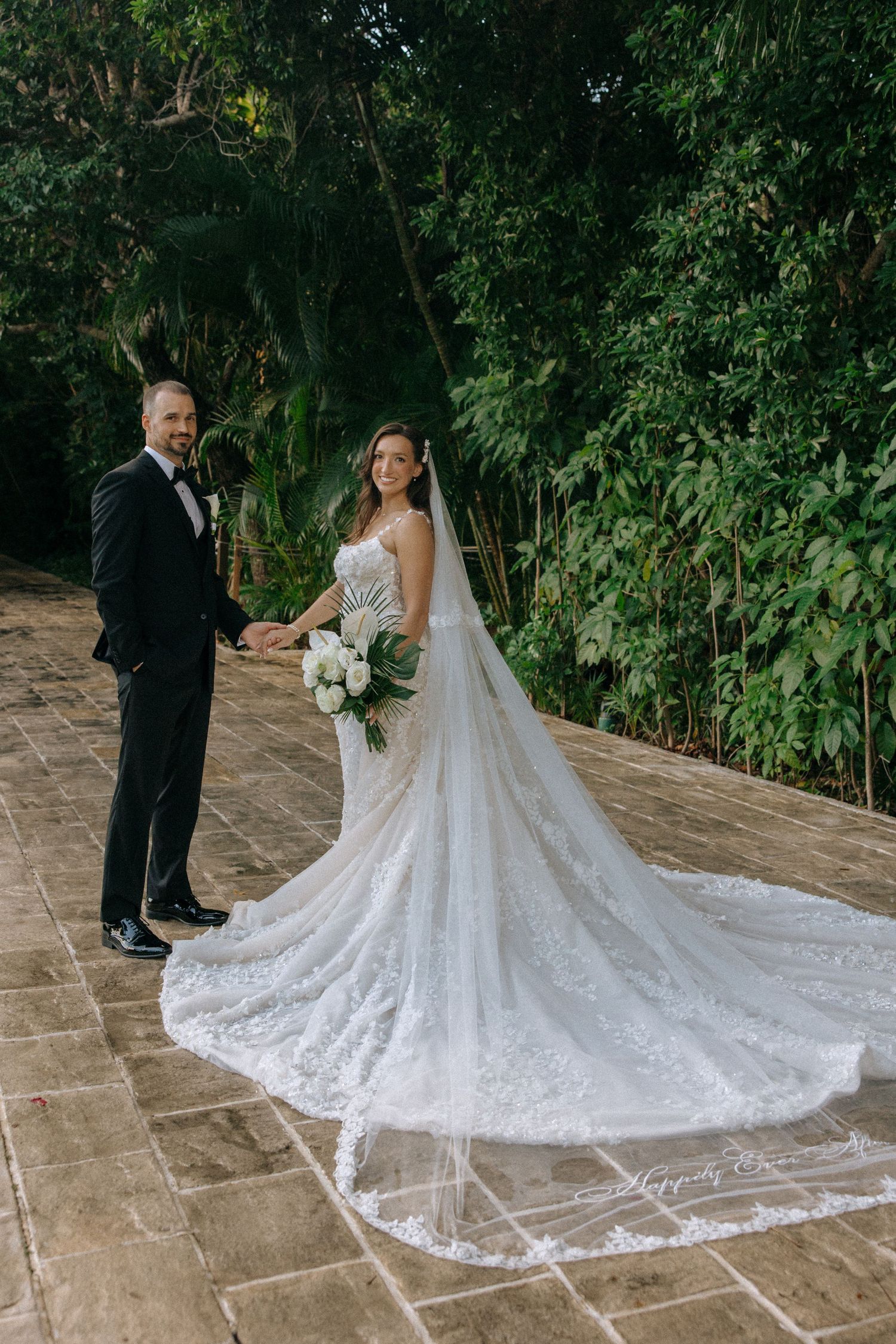 Wedding dress with intricate lace details and long train spreads across stone patio.
