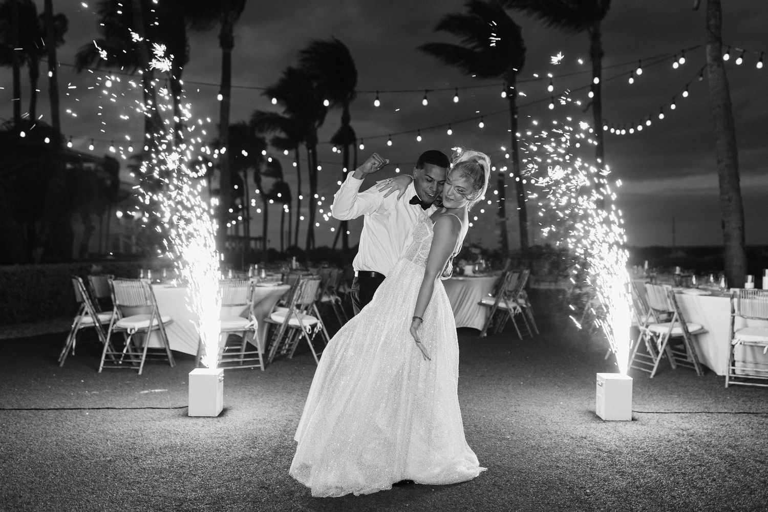 Black and white photo of sparklers creating light trails during an outdoor nighttime celebration.
