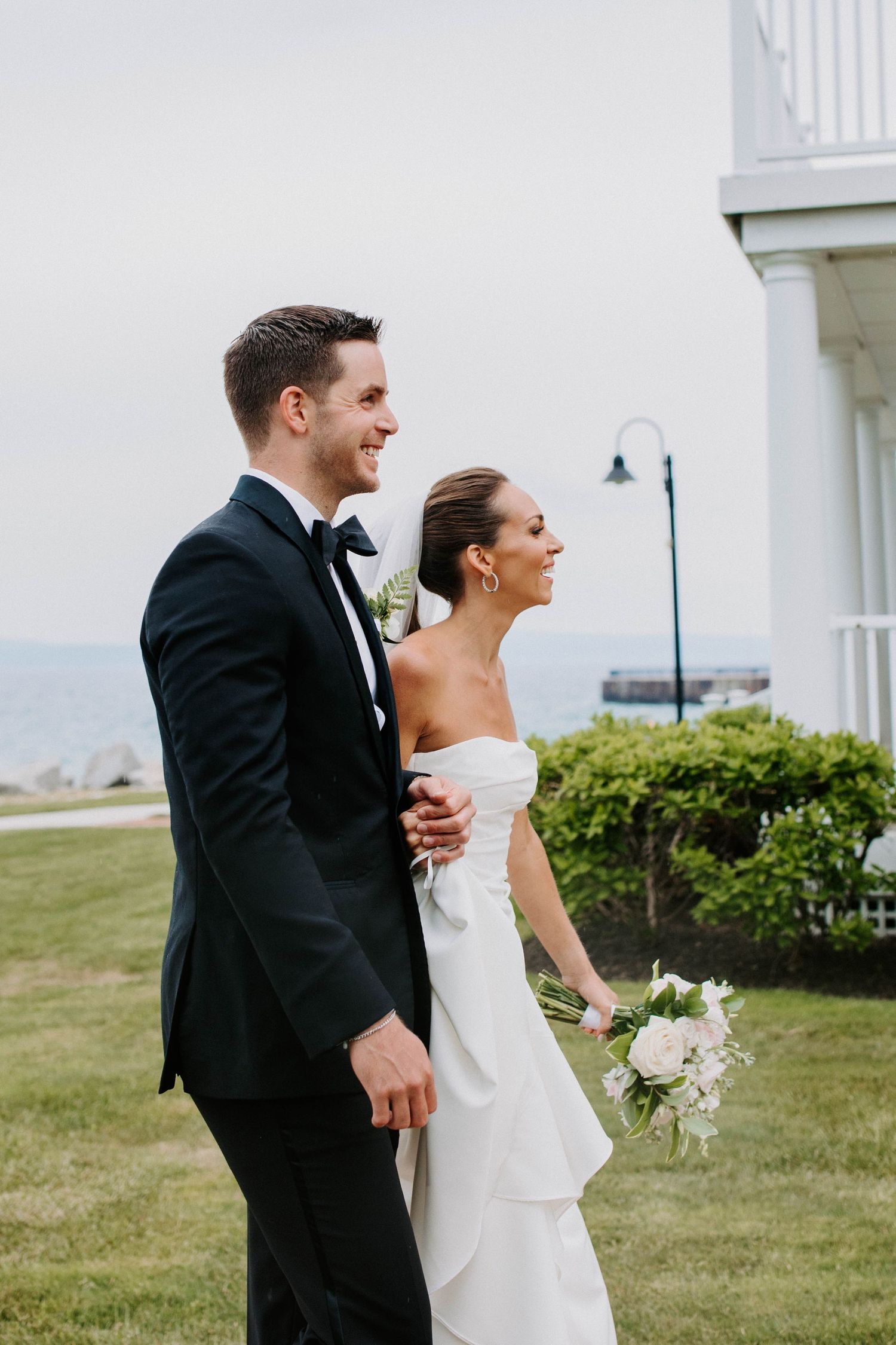 Candid laughter shared between newlyweds during outdoor coastal photoshoot.
