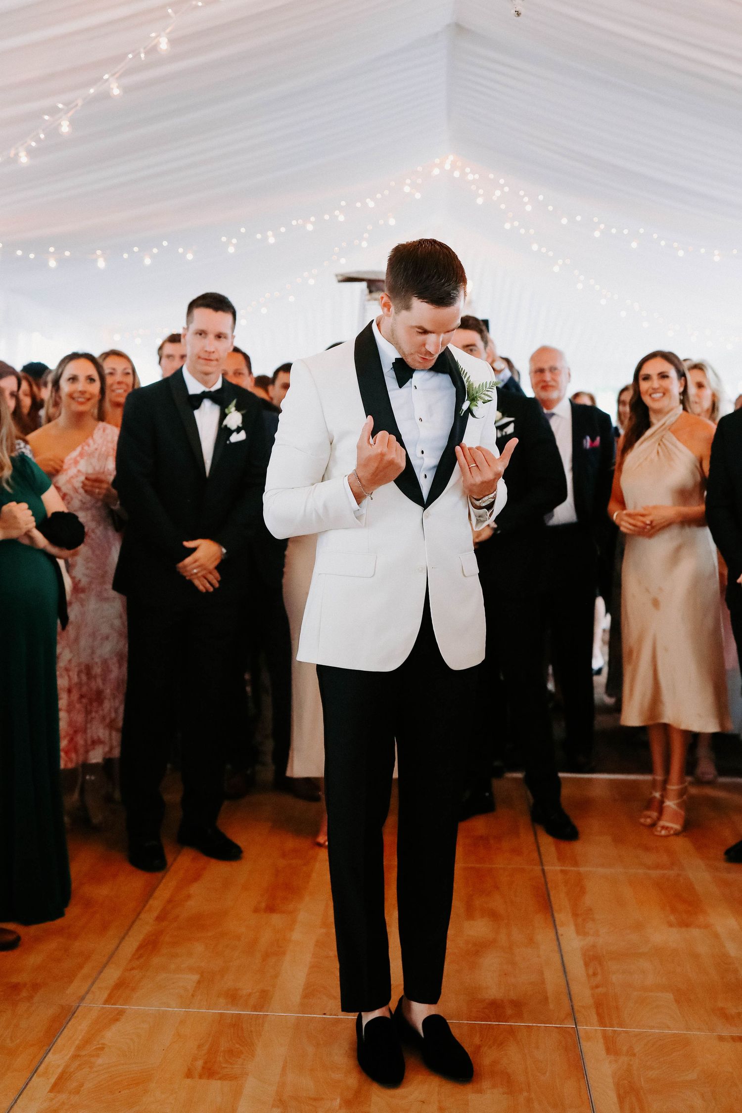 Formal wedding reception showing guests dancing on hardwood floors under elegant white tent ceiling.