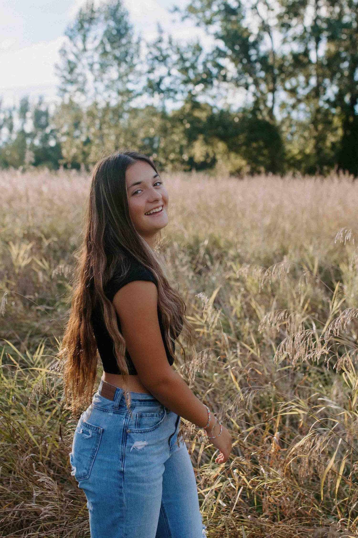 Candid poses in a sun-drenched field with casual denim and black top.