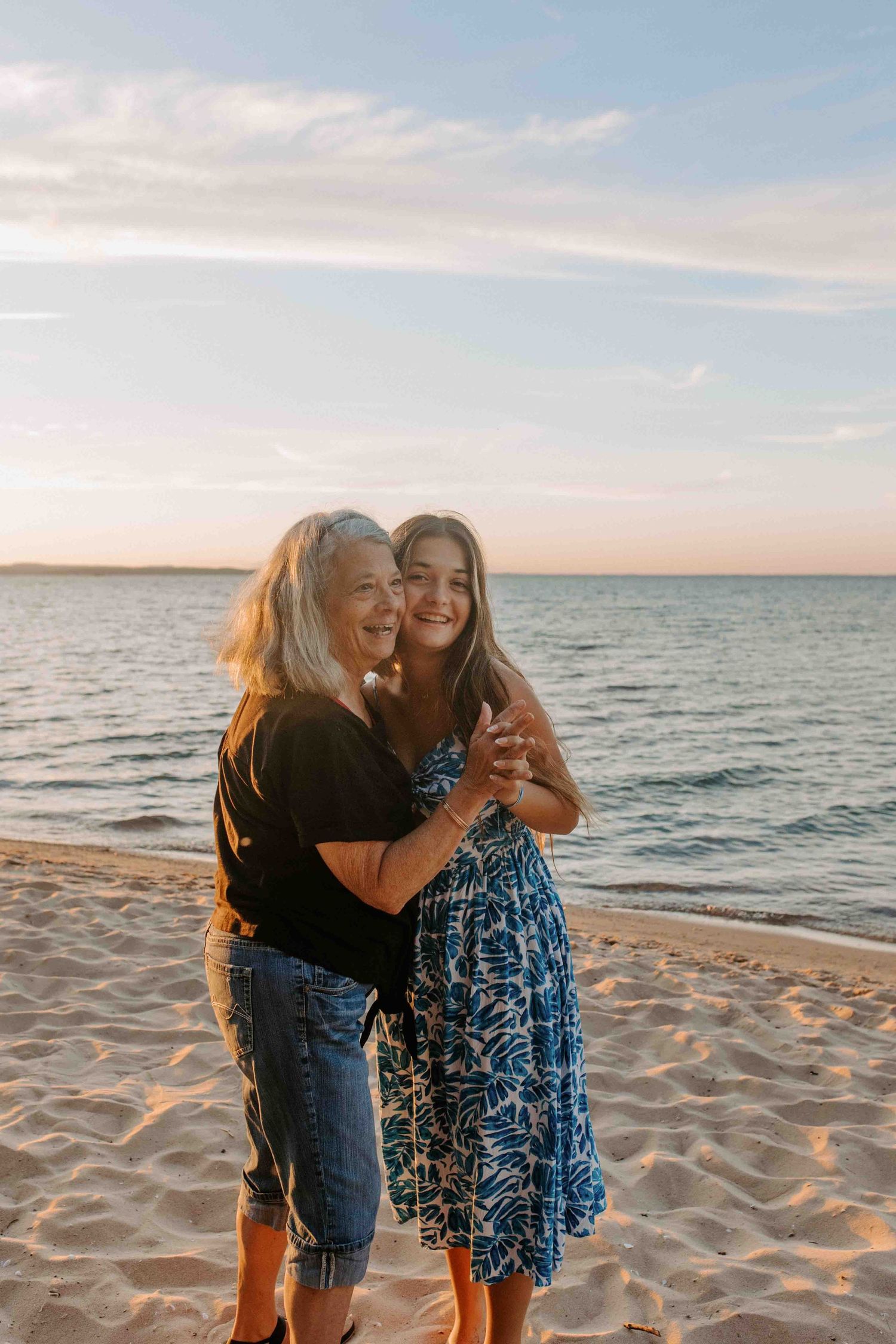 Two people embrace while sharing a candid moment on a beach at dusk.