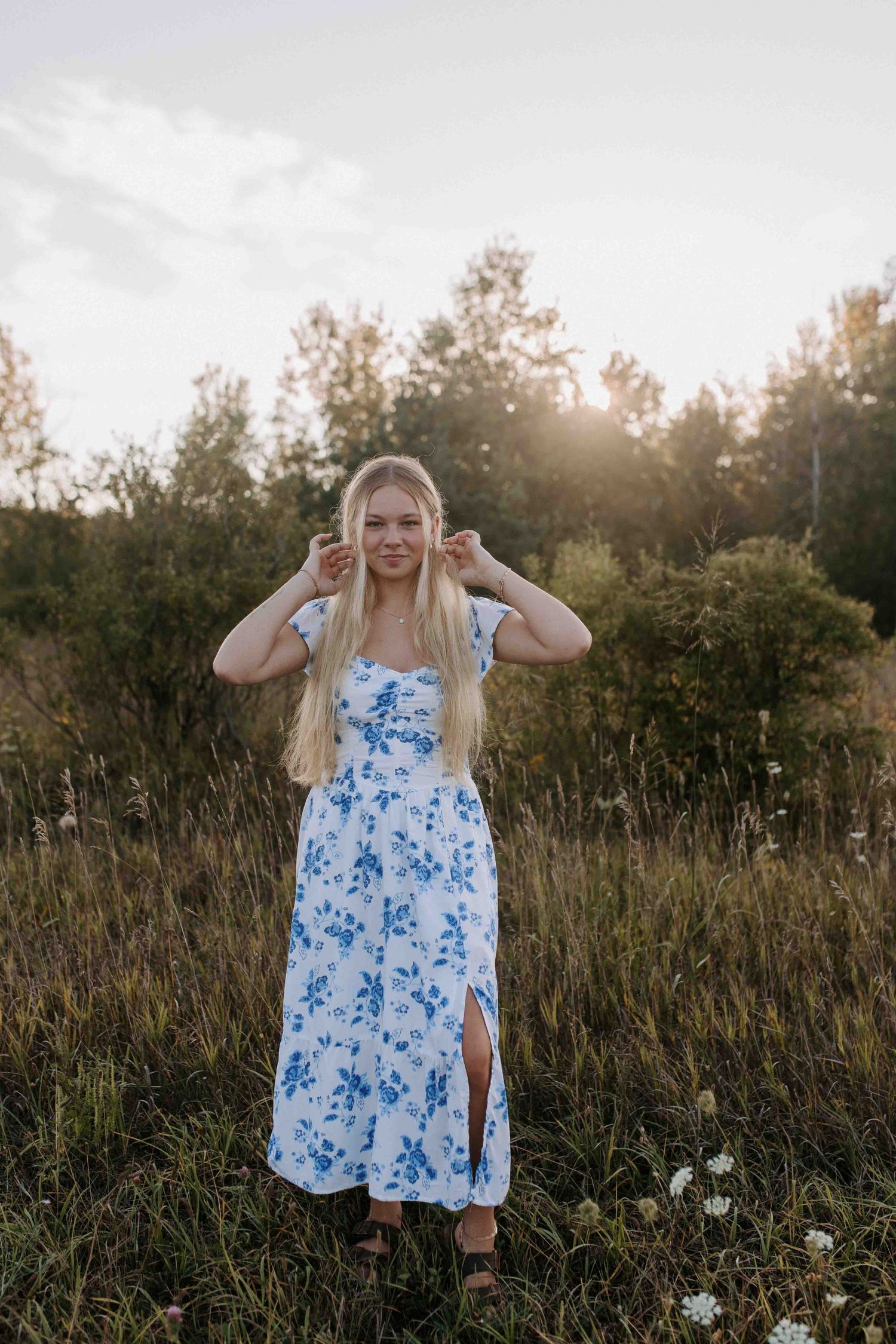 Candid outdoor portrait showing a flowing blue floral dress in a sunlit meadow.