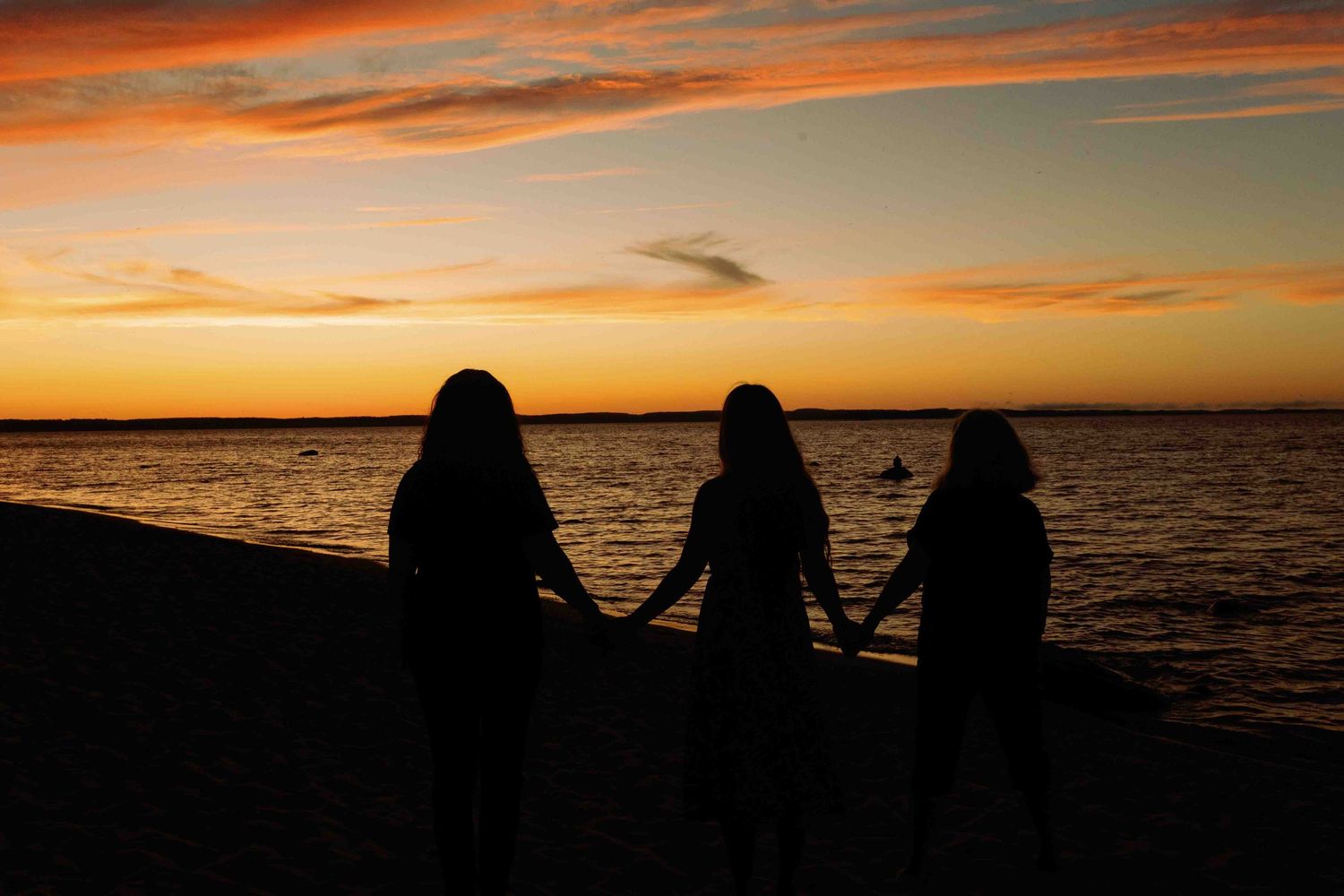 Silhouettes of people watching a vibrant orange sunset over the water.