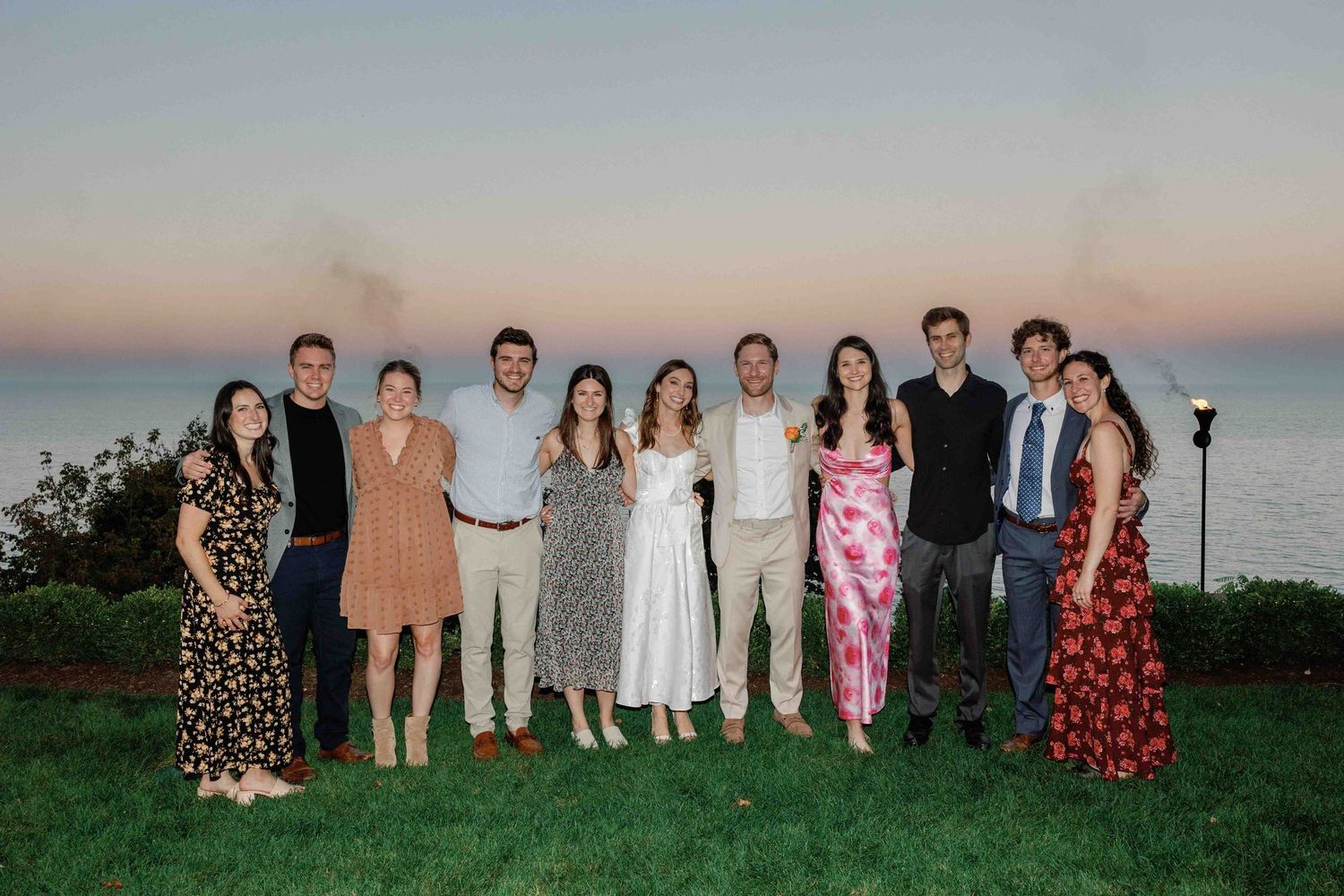 A group portrait of wedding guests standing together at sunset outdoors.