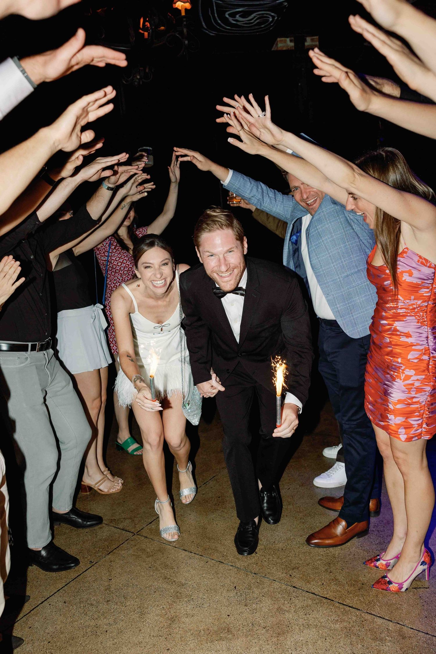 Party guests dance energetically in a dimly lit venue with decorative ceiling patterns.