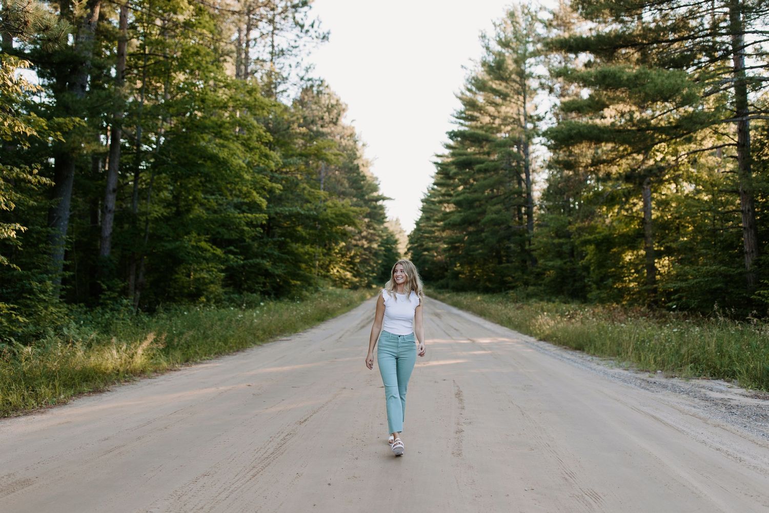 Person walking down tree-lined rural road during autumn.