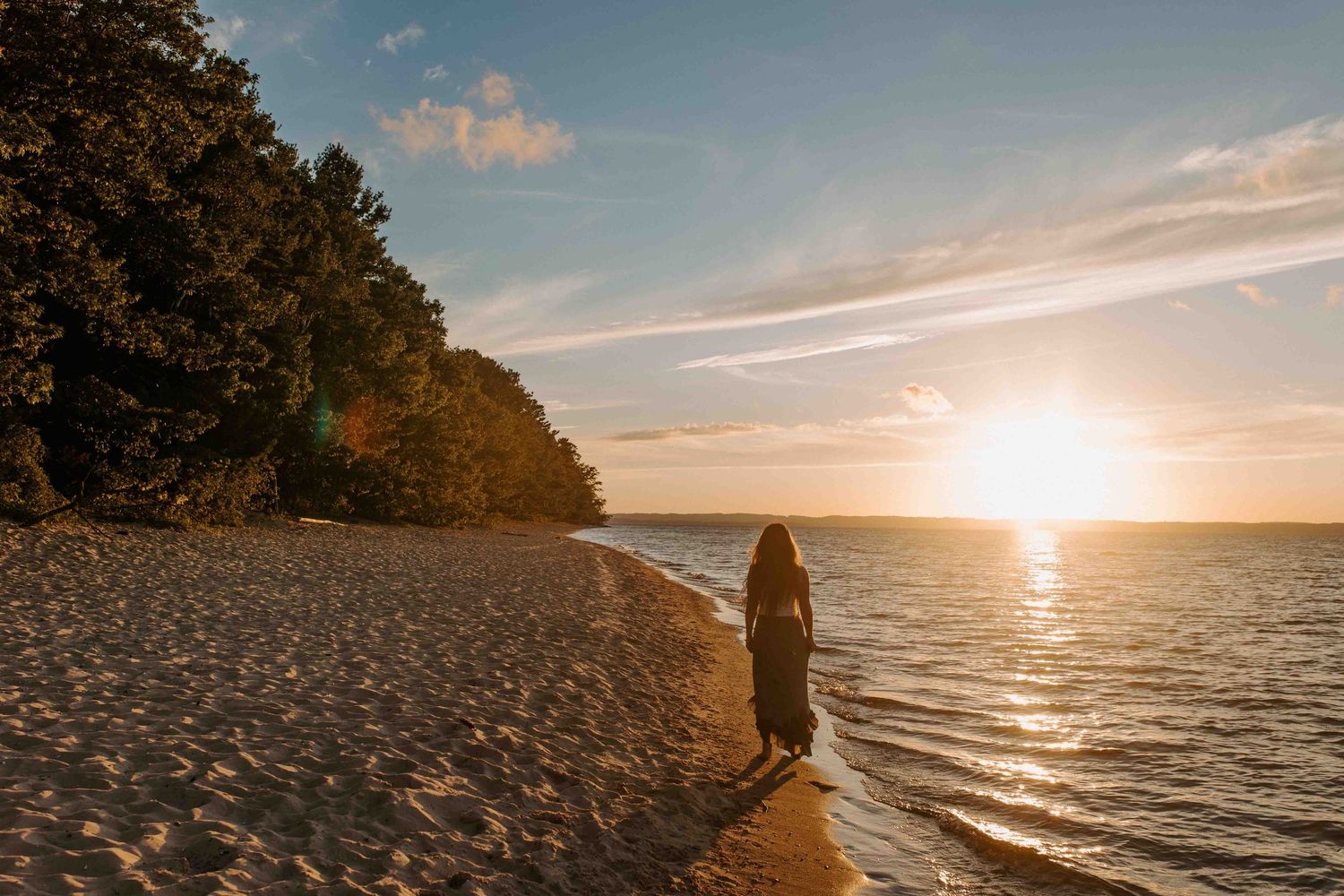 Silhouette of a person standing on a beach during sunset with dramatic golden light on the horizon.