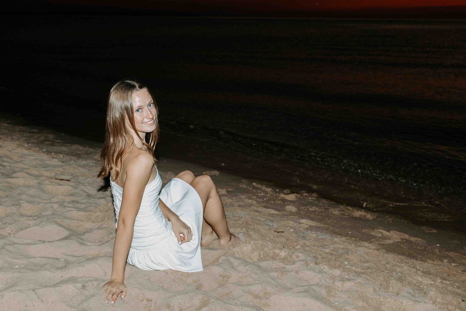 Person in white relaxes on the beach sand during golden hour.