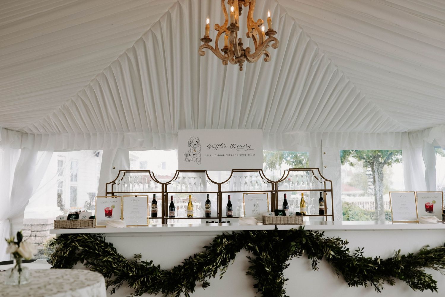 Large white wedding tent interior with elegant chandeliers and draped fabric ceiling.