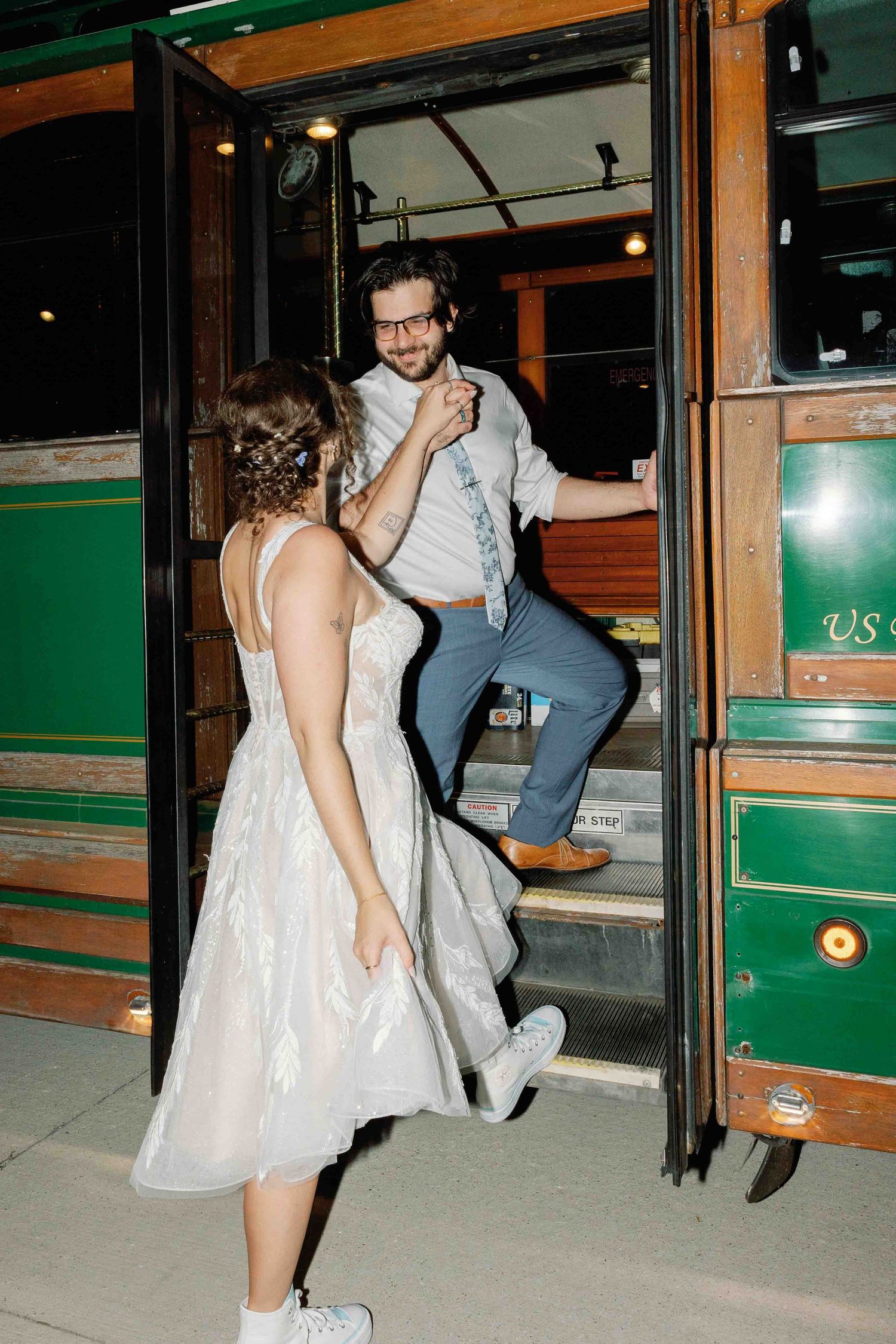 Couple in formal attire boarding a vintage green trolley car at night.
