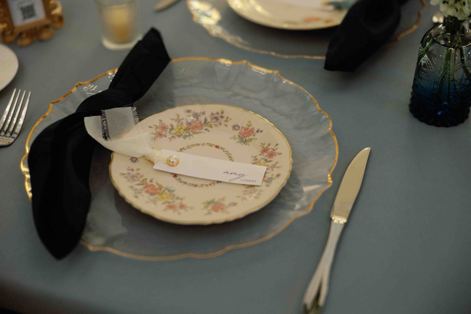 Elegant place settings with vintage plates and gold trim on a dark tablecloth.