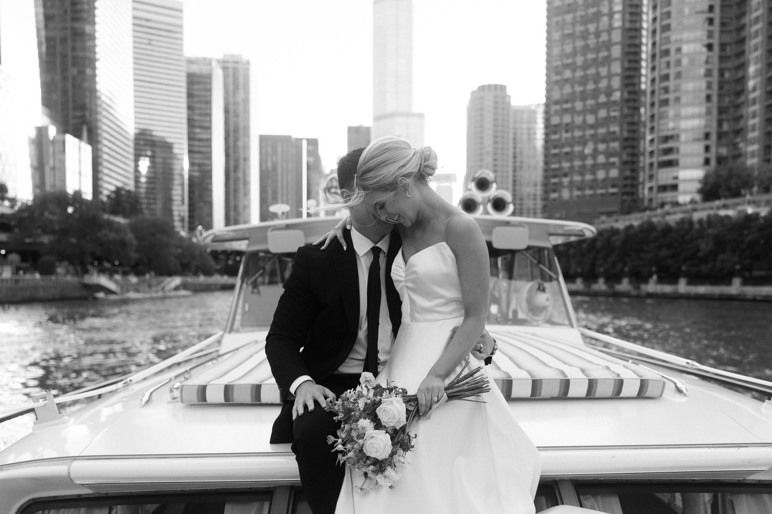 A romantic couple in formal attire poses together on a city rooftop with skyscrapers in the background.