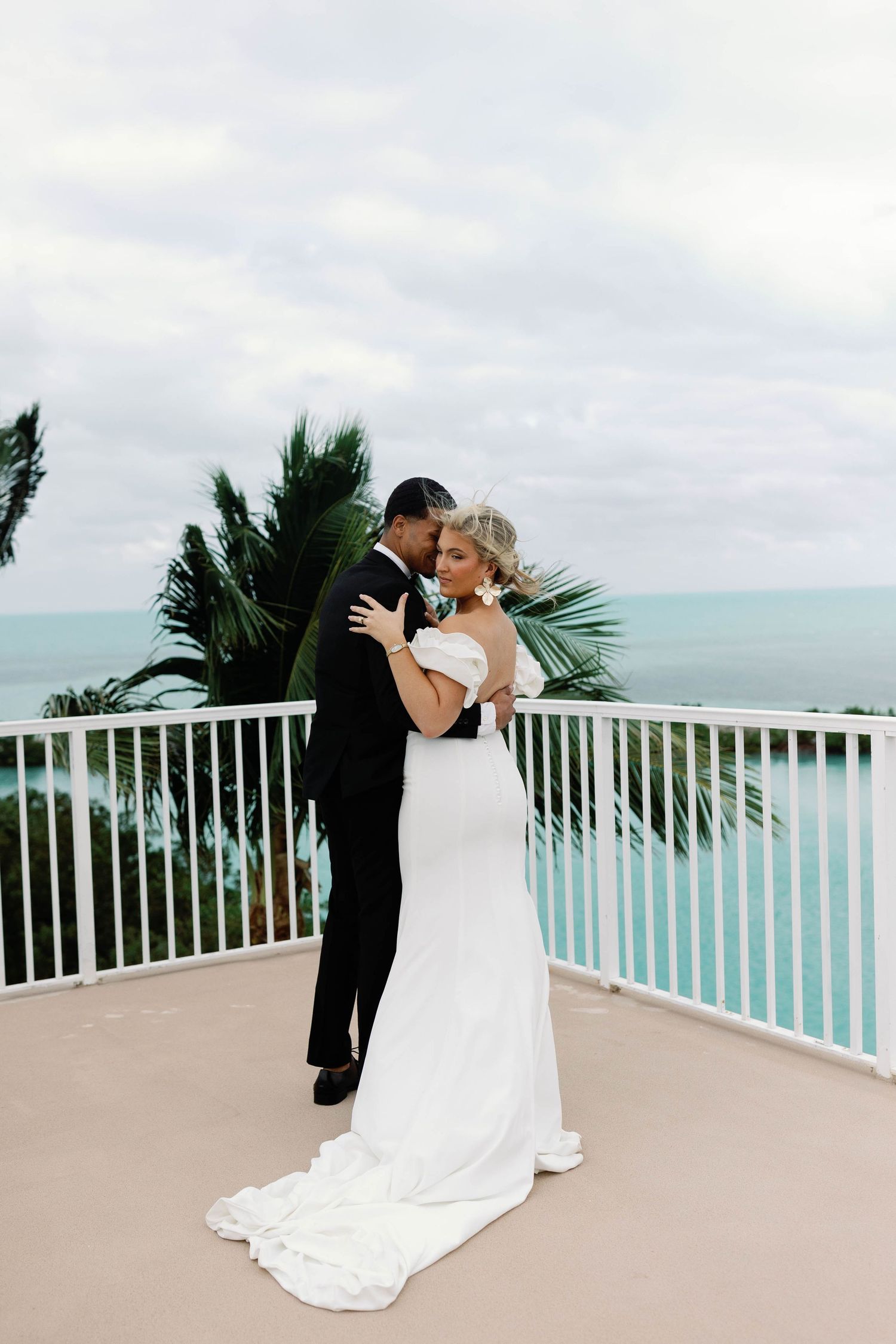 A romantic beach wedding ceremony on a balcony overlooking turquoise waters with palm trees swaying in the breeze.