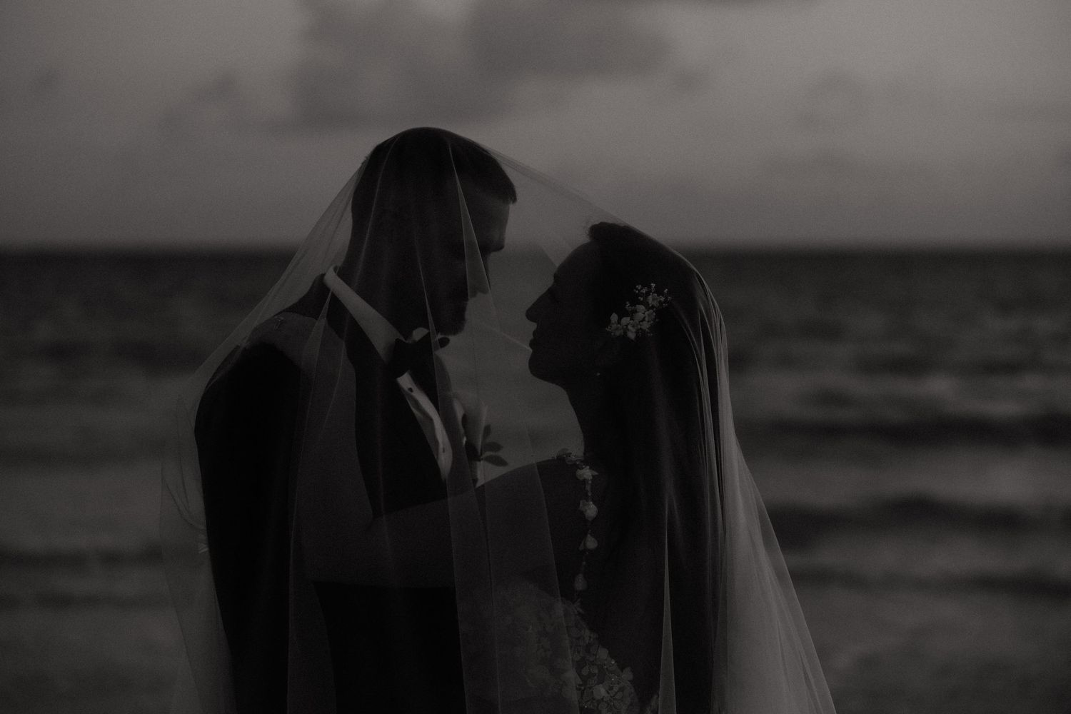 A romantic silhouette of a couple against a moody ocean backdrop at sunset.