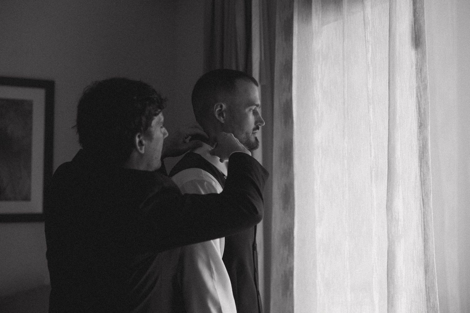Black and white photo showing silhouettes near a window during wedding preparations.