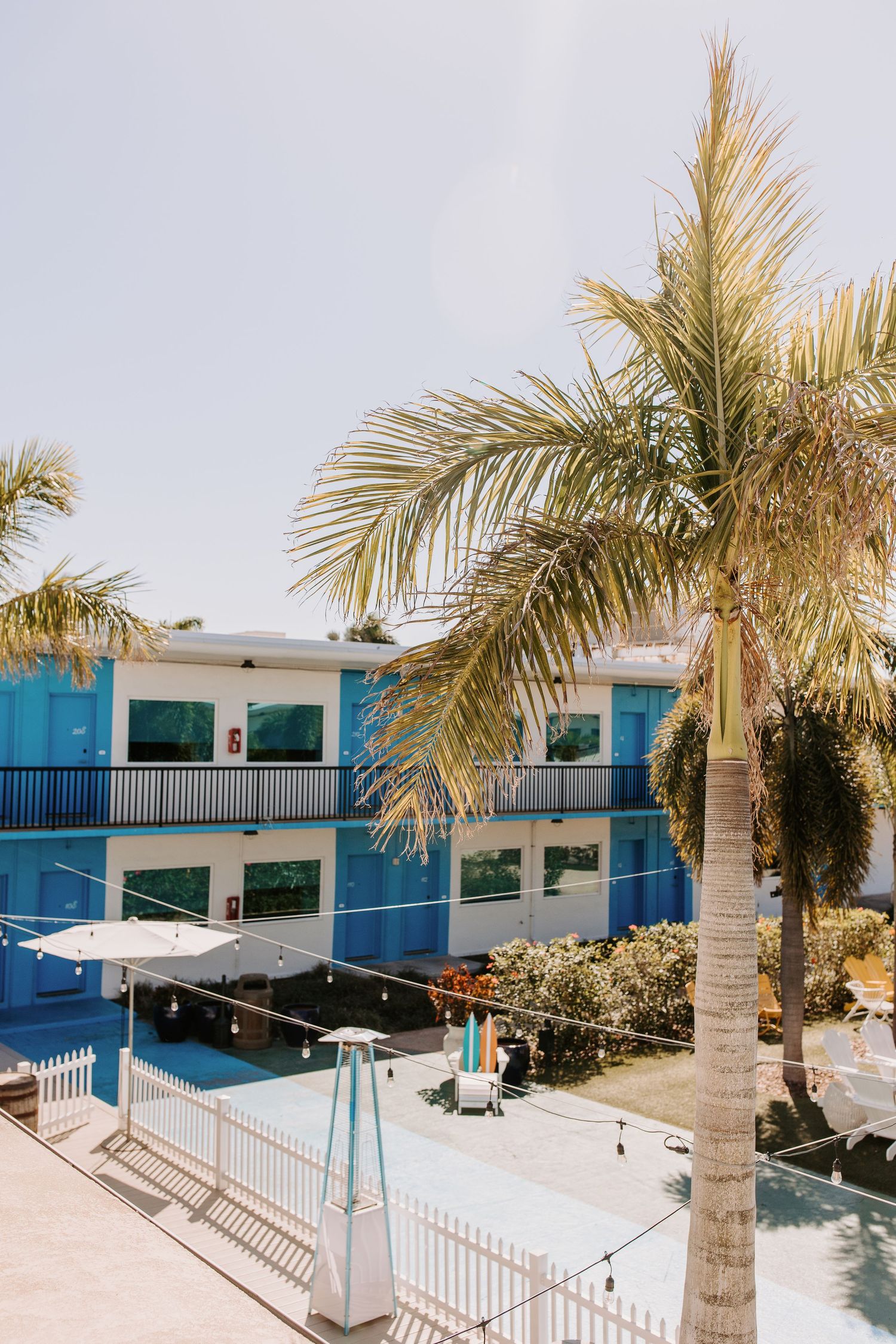 Bright blue motel building with palm trees and swimming pool in a sunny tropical setting.