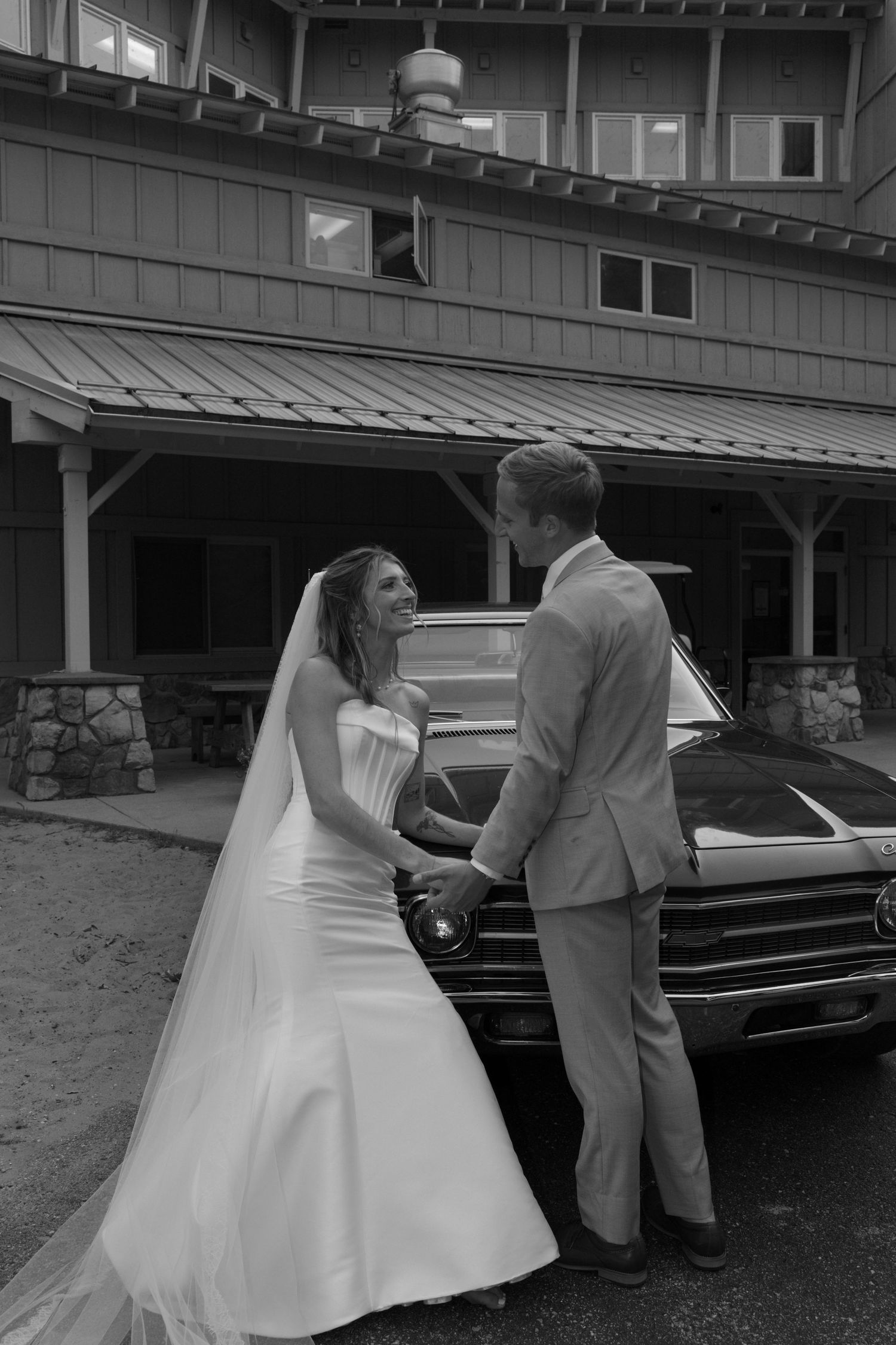 Wedding couple standing together near parked vintage cars outside a building.