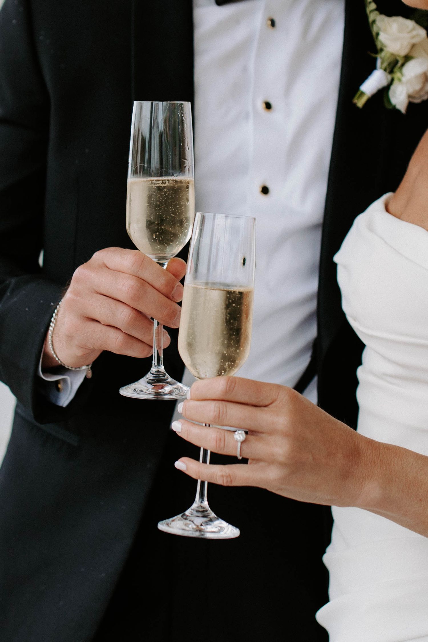 Close-up of champagne glasses being held by wedding party members in formal attire.