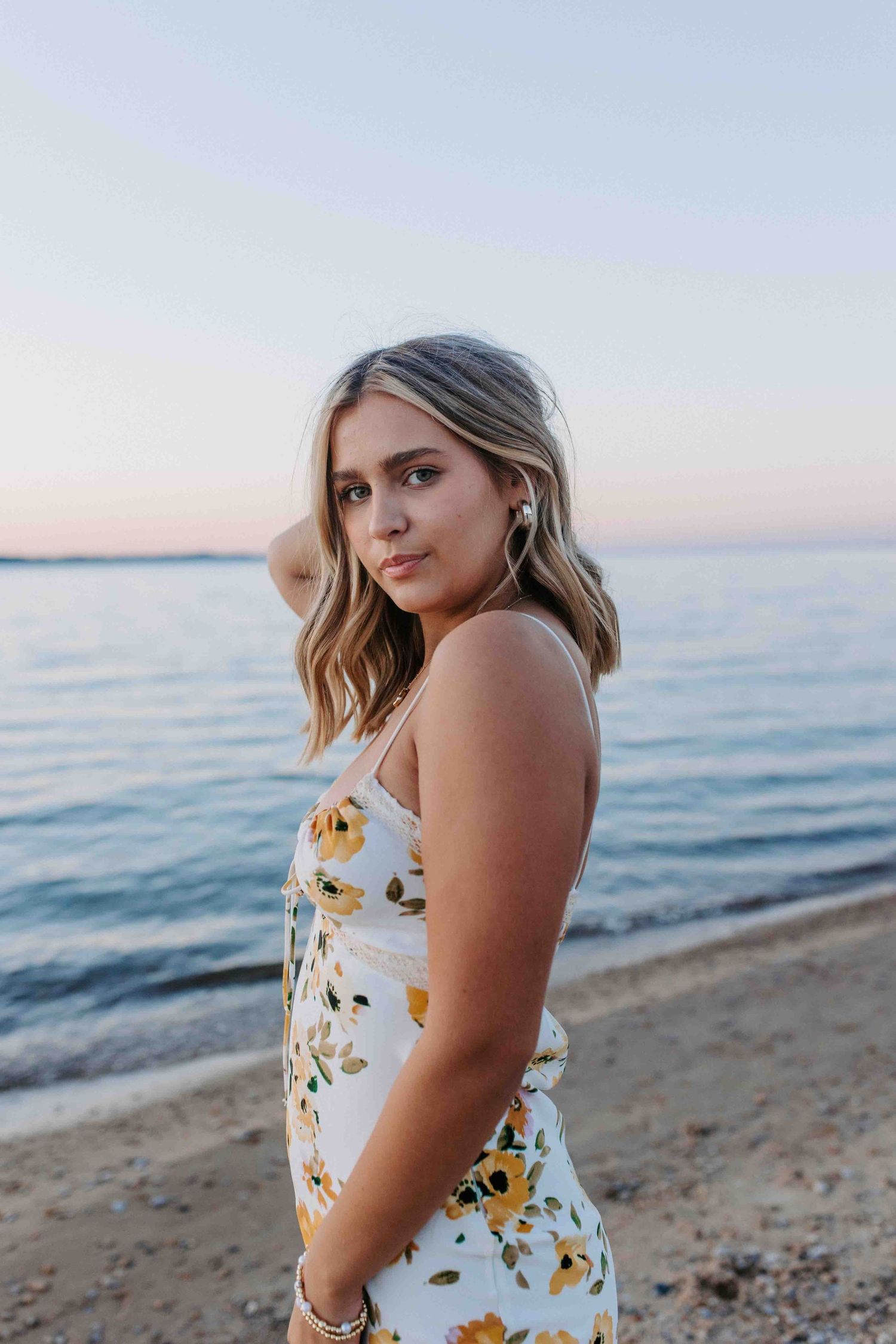 A person in a floral summer dress poses against a sunset beach backdrop.