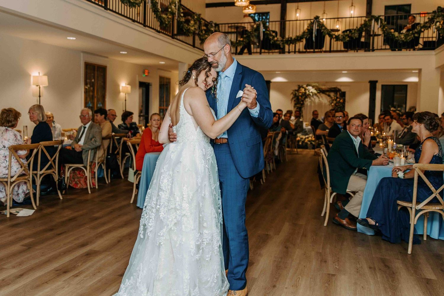 Wedding guests dance and celebrate on a wooden dance floor at an elegant indoor reception venue.