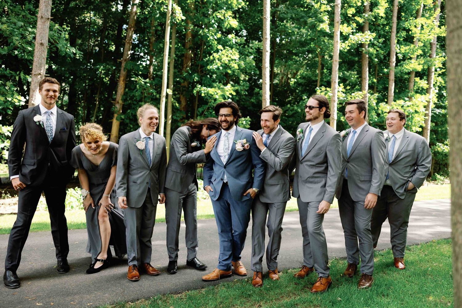 Groomsmen in matching gray suits pose together on a wooded path.