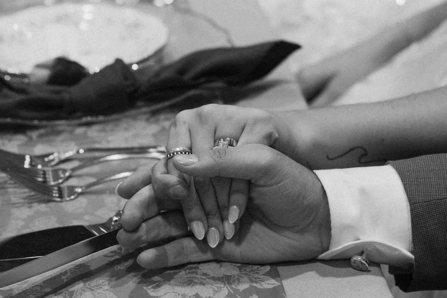 A black and white close-up of hands with wedding rings.