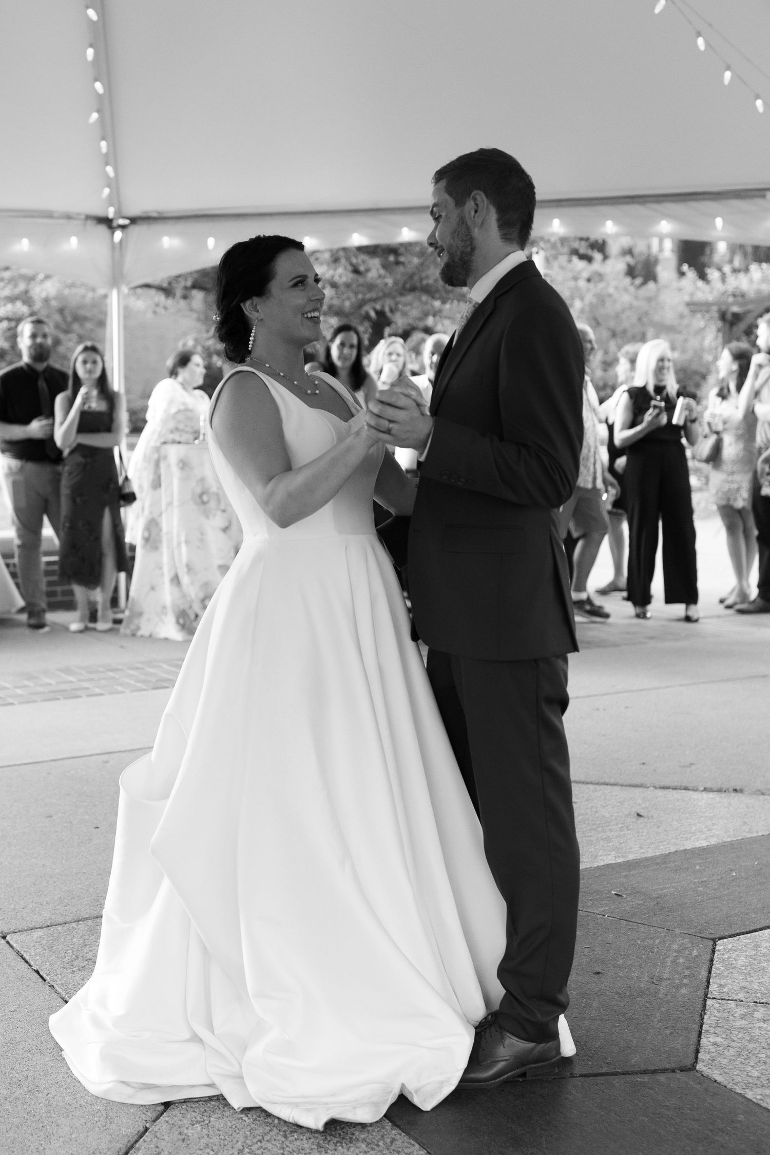 A couple shares their first dance under a white tent at their wedding reception.
