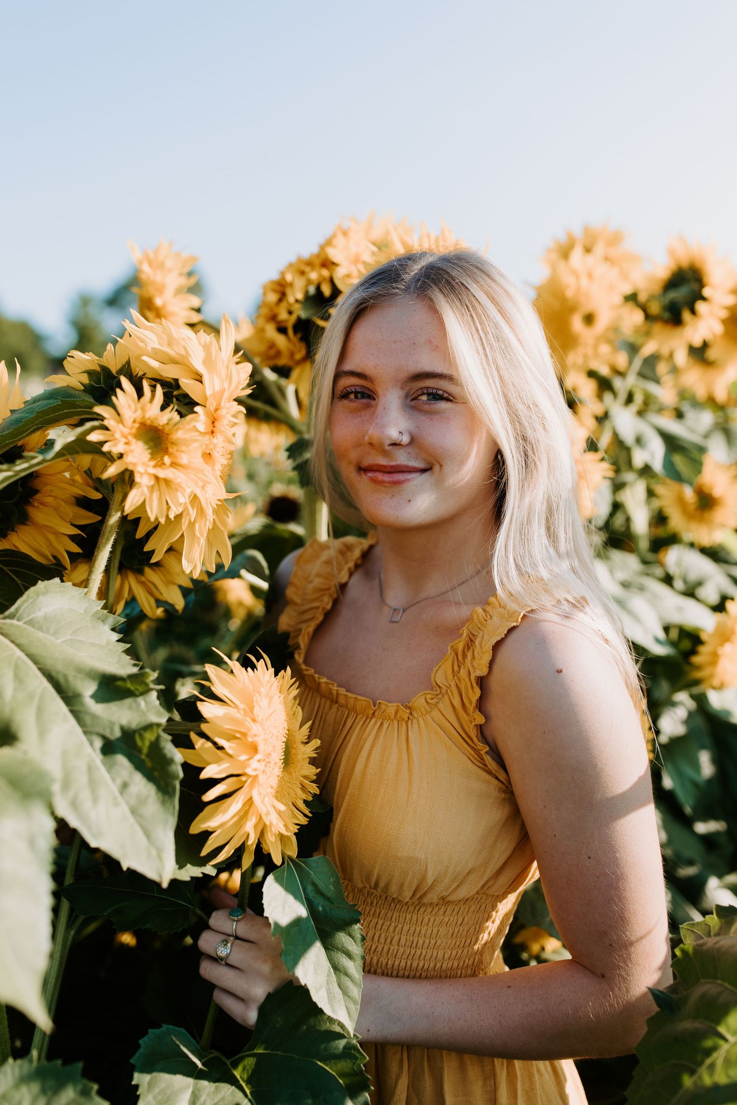 Person in yellow top poses among blooming sunflowers in summer field.