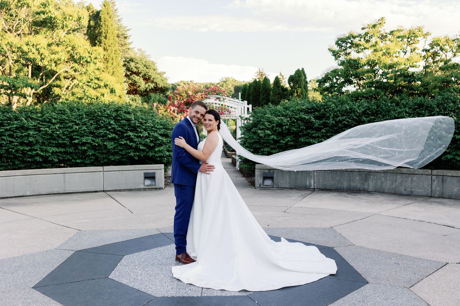 Elegant wedding couple walking and posing on outdoor patio with flowing white dress.