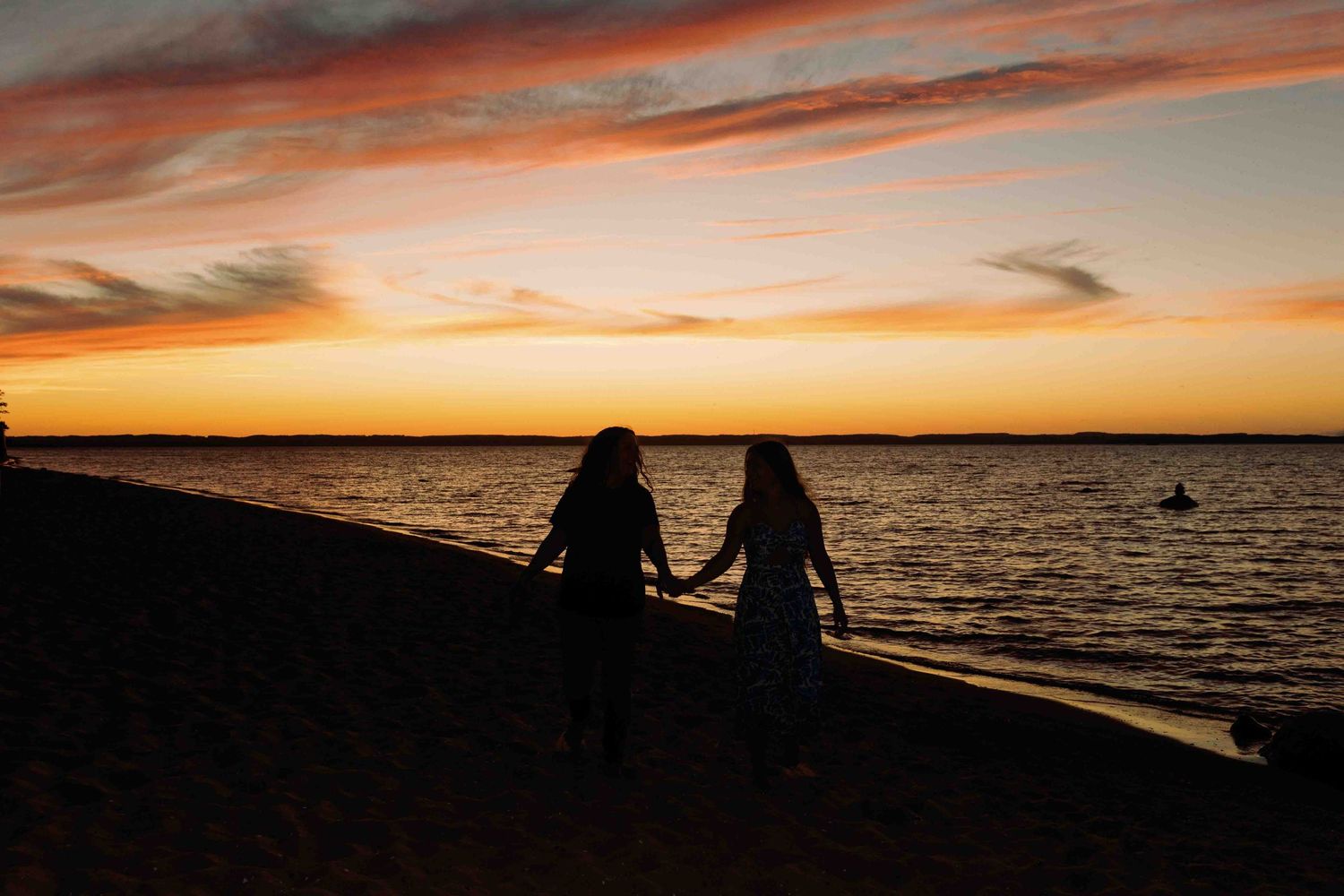Figures watching the sunset on a beach with vibrant orange and yellow sky.